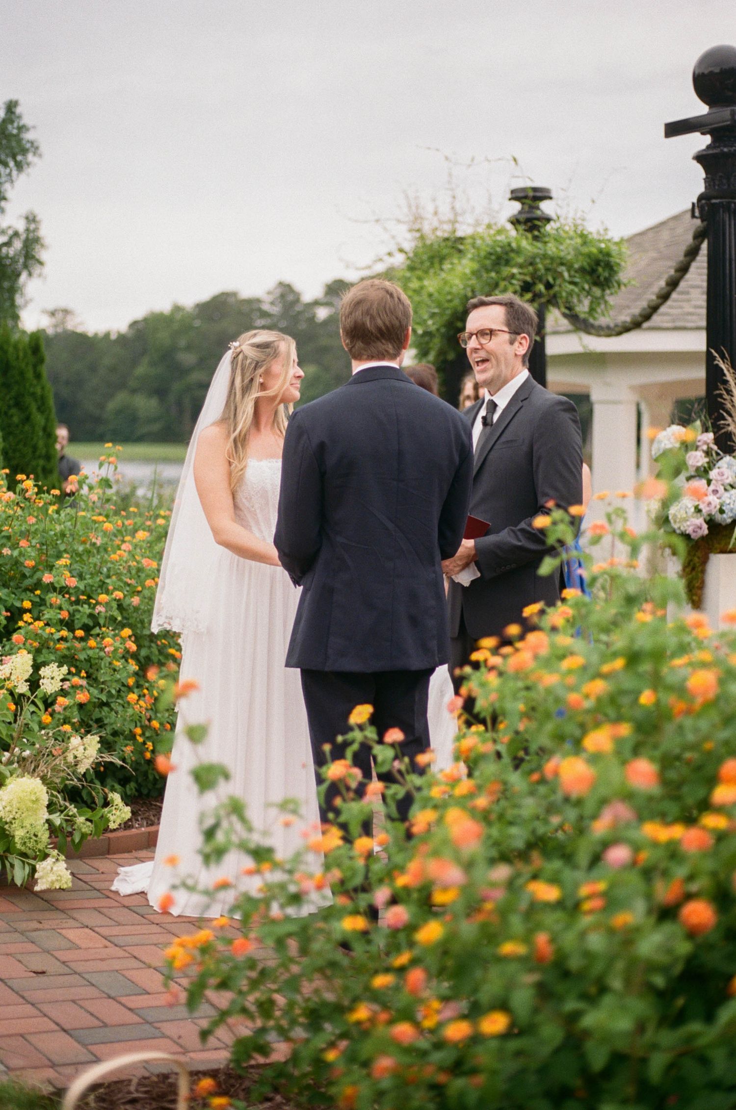 Bride and groom exchange vows outdoors surrounded by vibrant orange and yellow flowers at a garden wedding ceremony.
