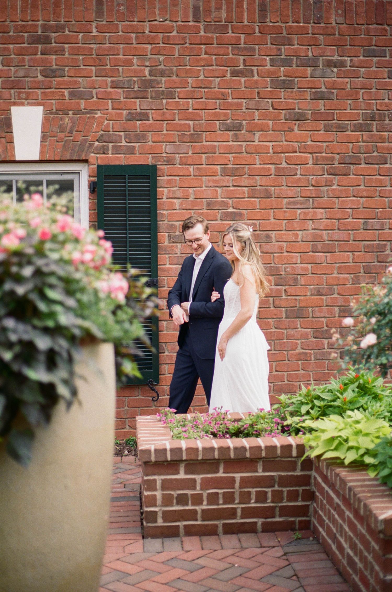 Bride and groom share quiet moment on brick steps beside red brick building with flowers.