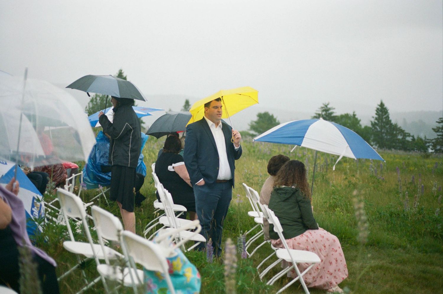 Wedding guests with colorful umbrellas gather outdoors for a celebration.