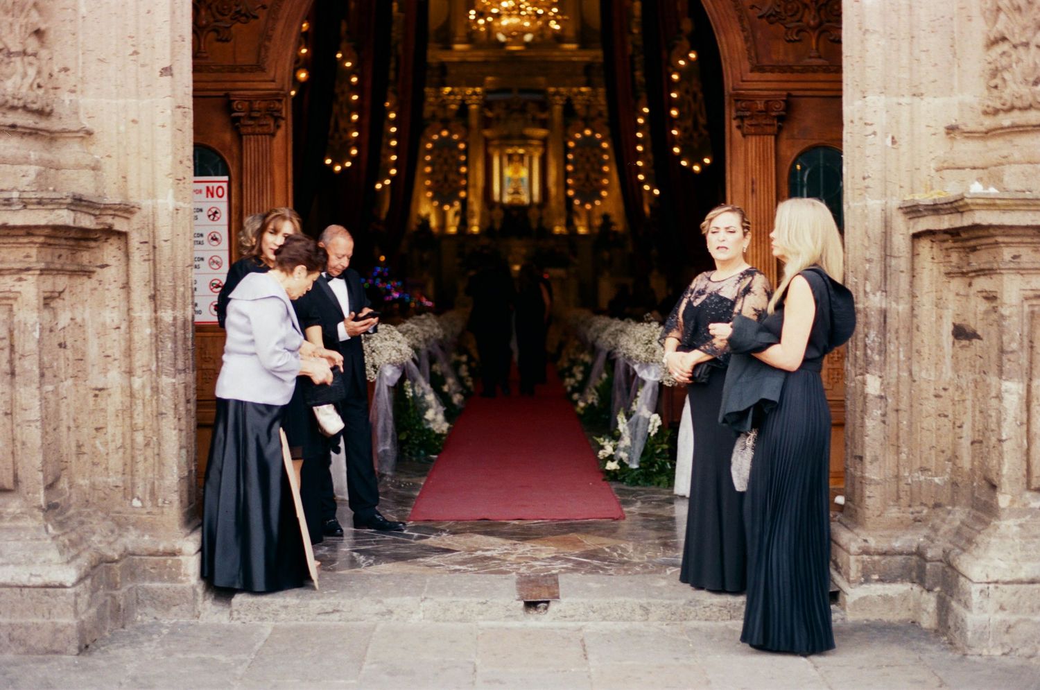 Wedding ceremony entrance at an ornate stone church with attendees in formal attire.