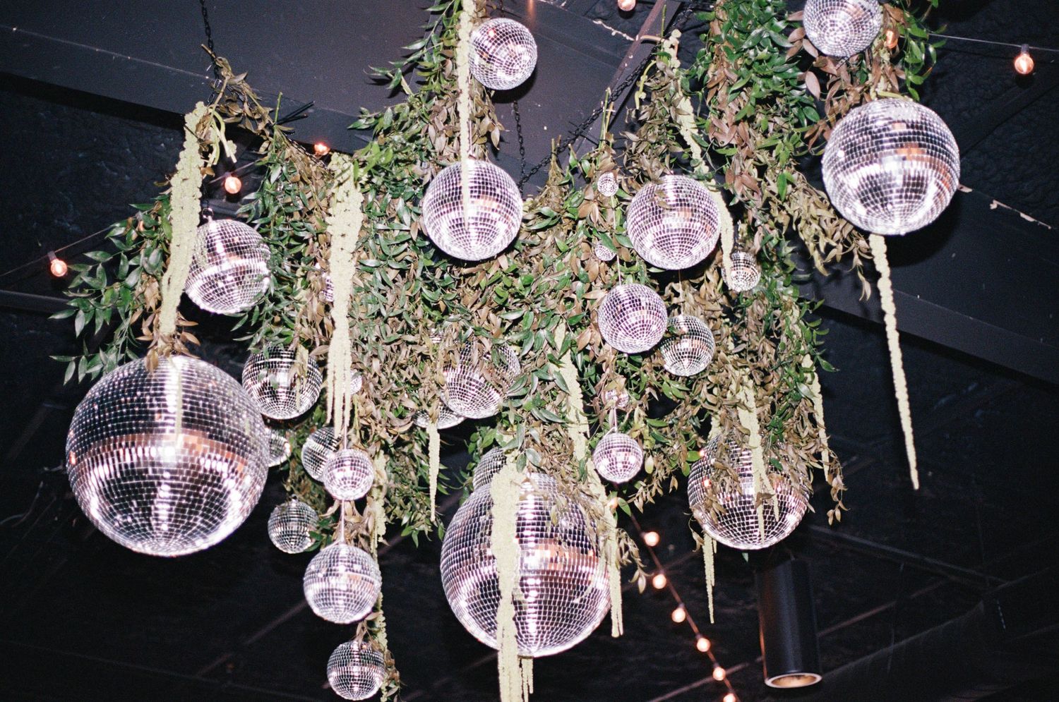 Decorative glass orbs and greenery hang from the ceiling at an evening wedding reception.