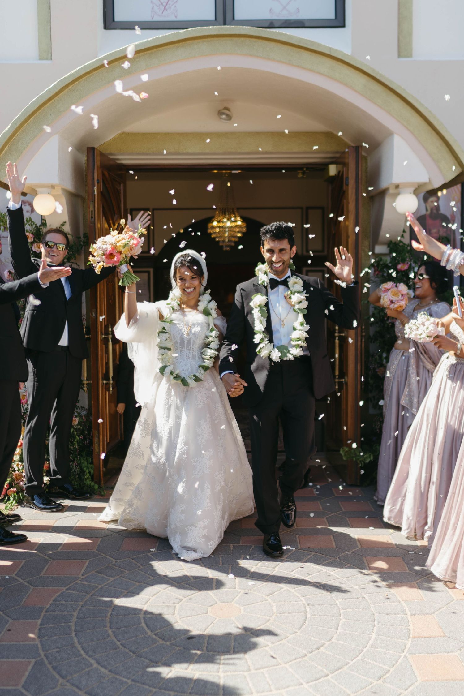 Joyful newlyweds exit church under confetti shower as guests celebrate their wedding ceremony.