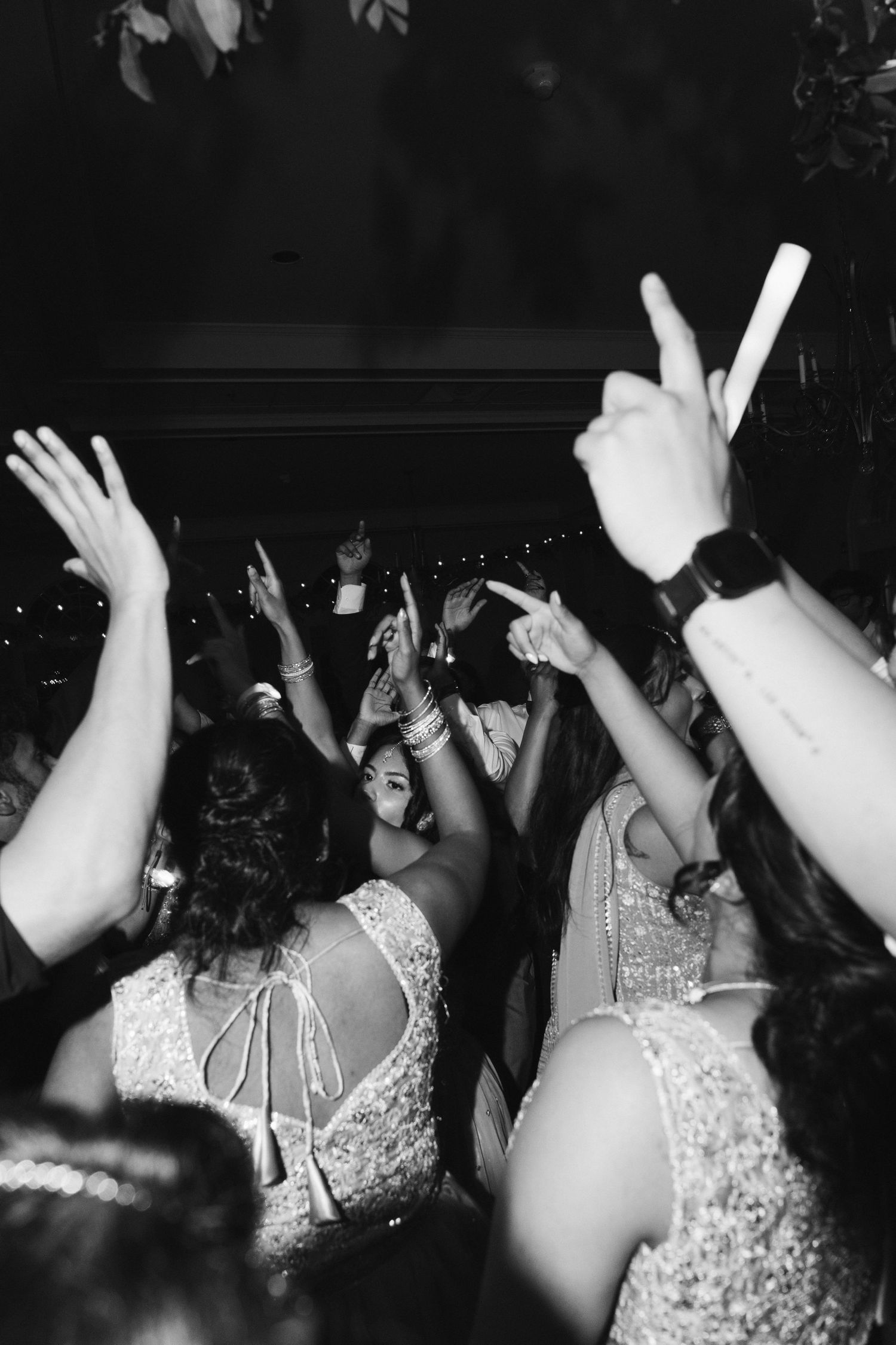 Black and white photo of women in elegant dresses dancing with raised arms at a festive celebration.