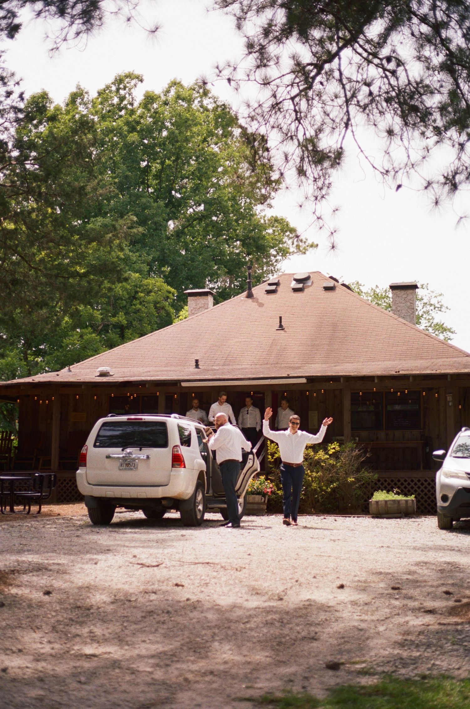 Guests arriving at a rustic wedding venue with a brown roof surrounded by trees.