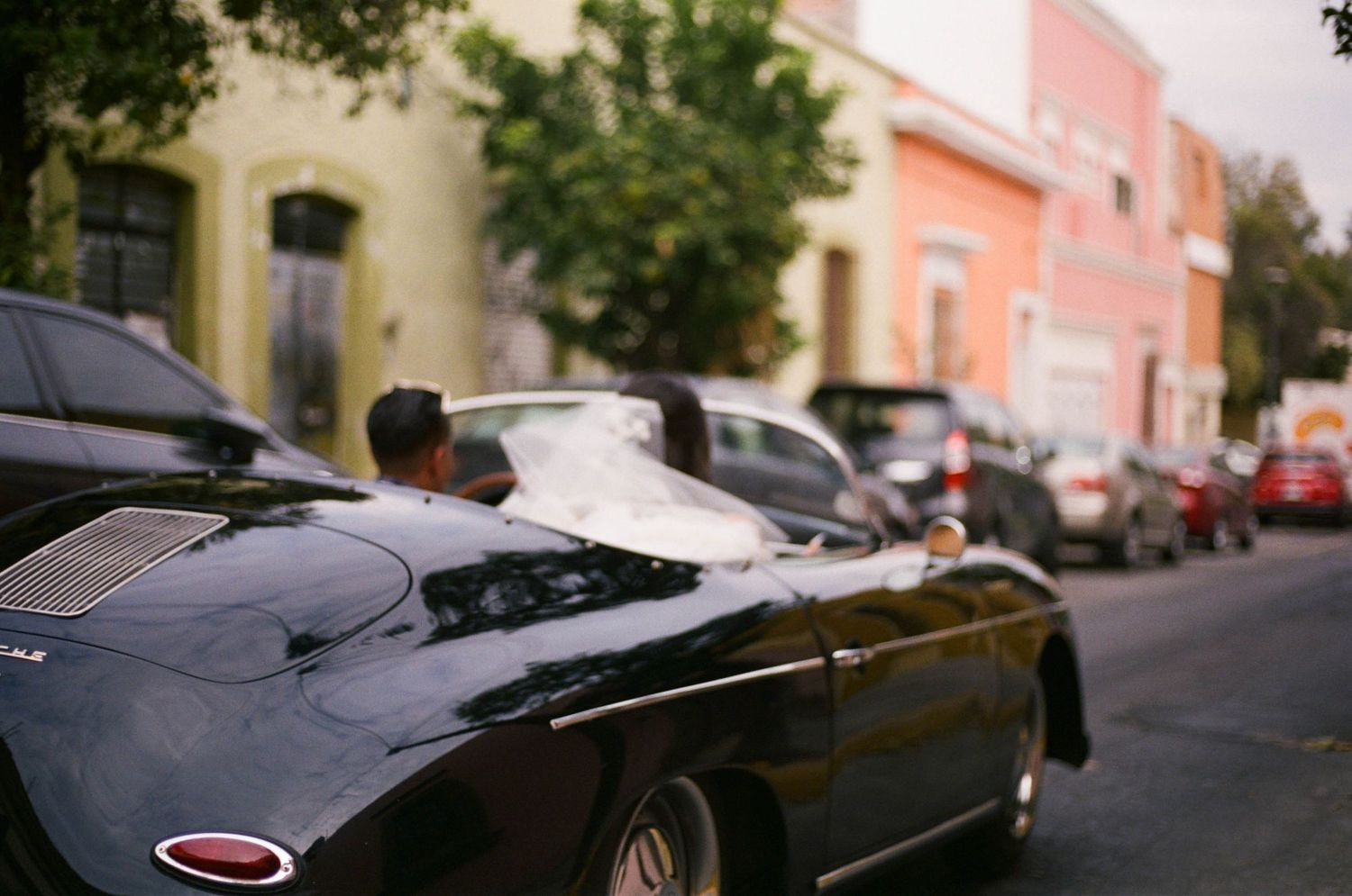 A sleek black vintage sports car parked on a street with pastel-colored buildings in the background.