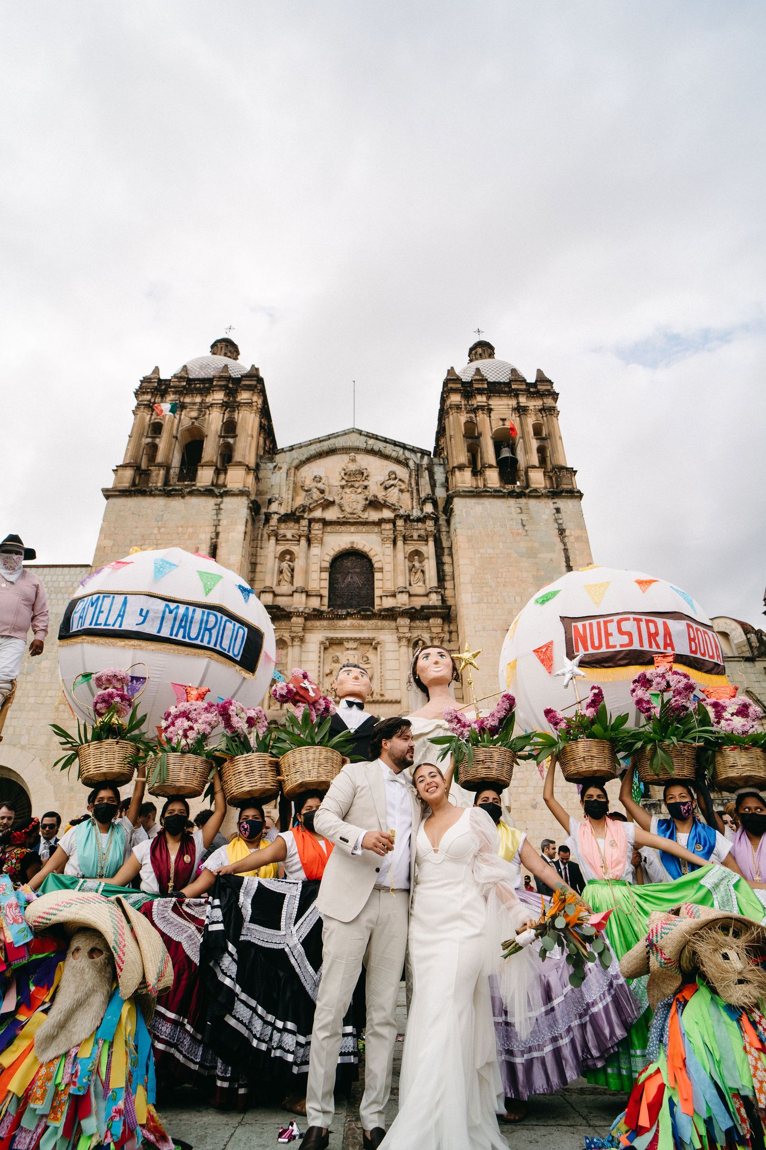 Wedding celebration outside ornate Mexican cathedral with festive balloons and traditional dancers.