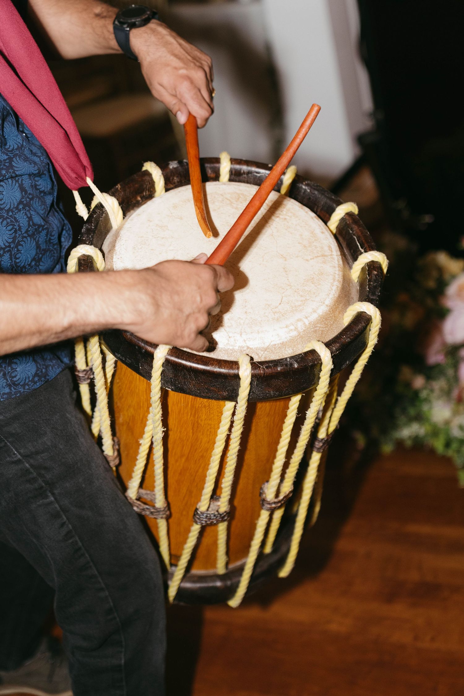 Musician playing a traditional wooden dhol drum with sticks at a wedding celebration event.
