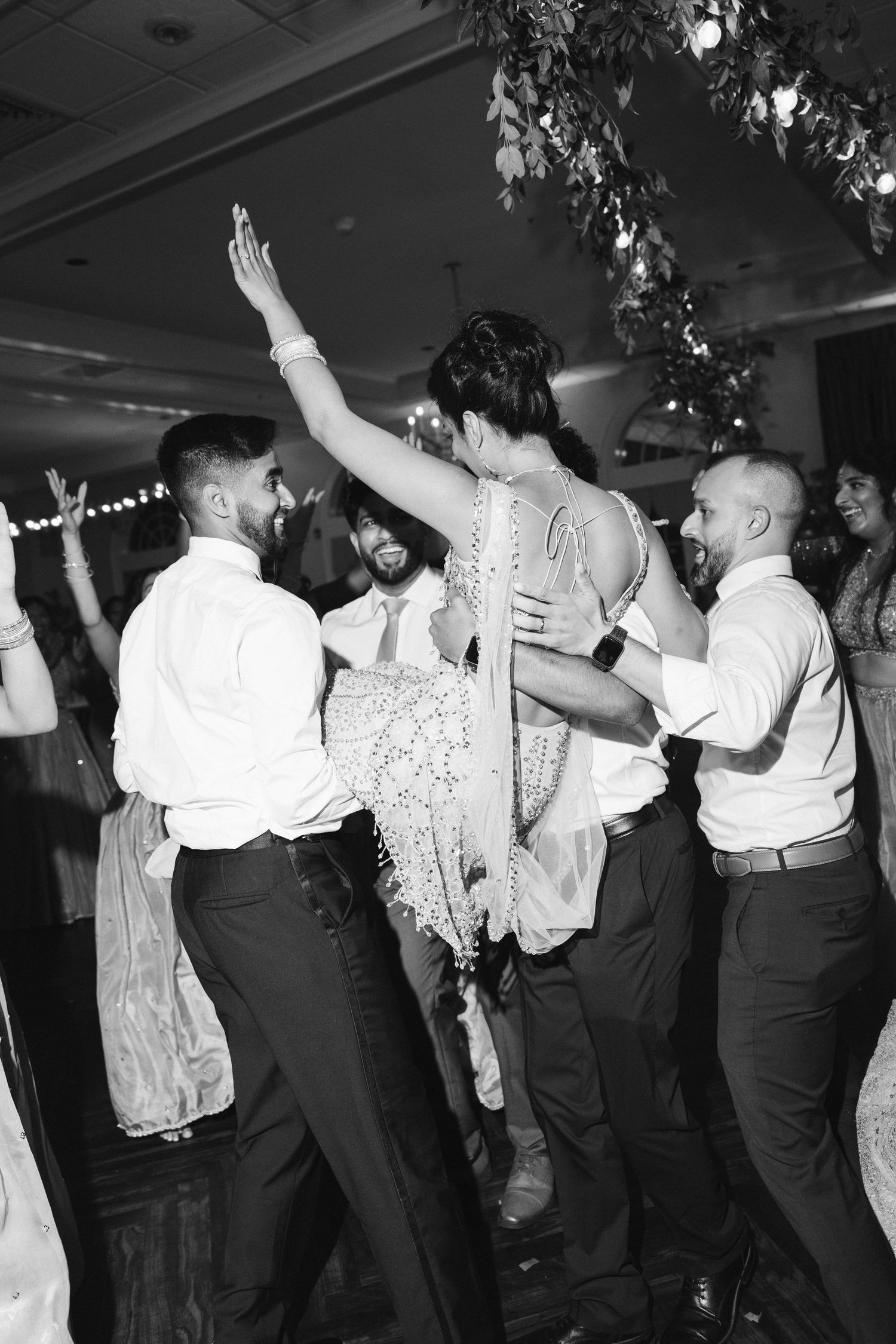 Bride dancing with groomsmen at wedding reception, black and white photo with festive atmosphere.