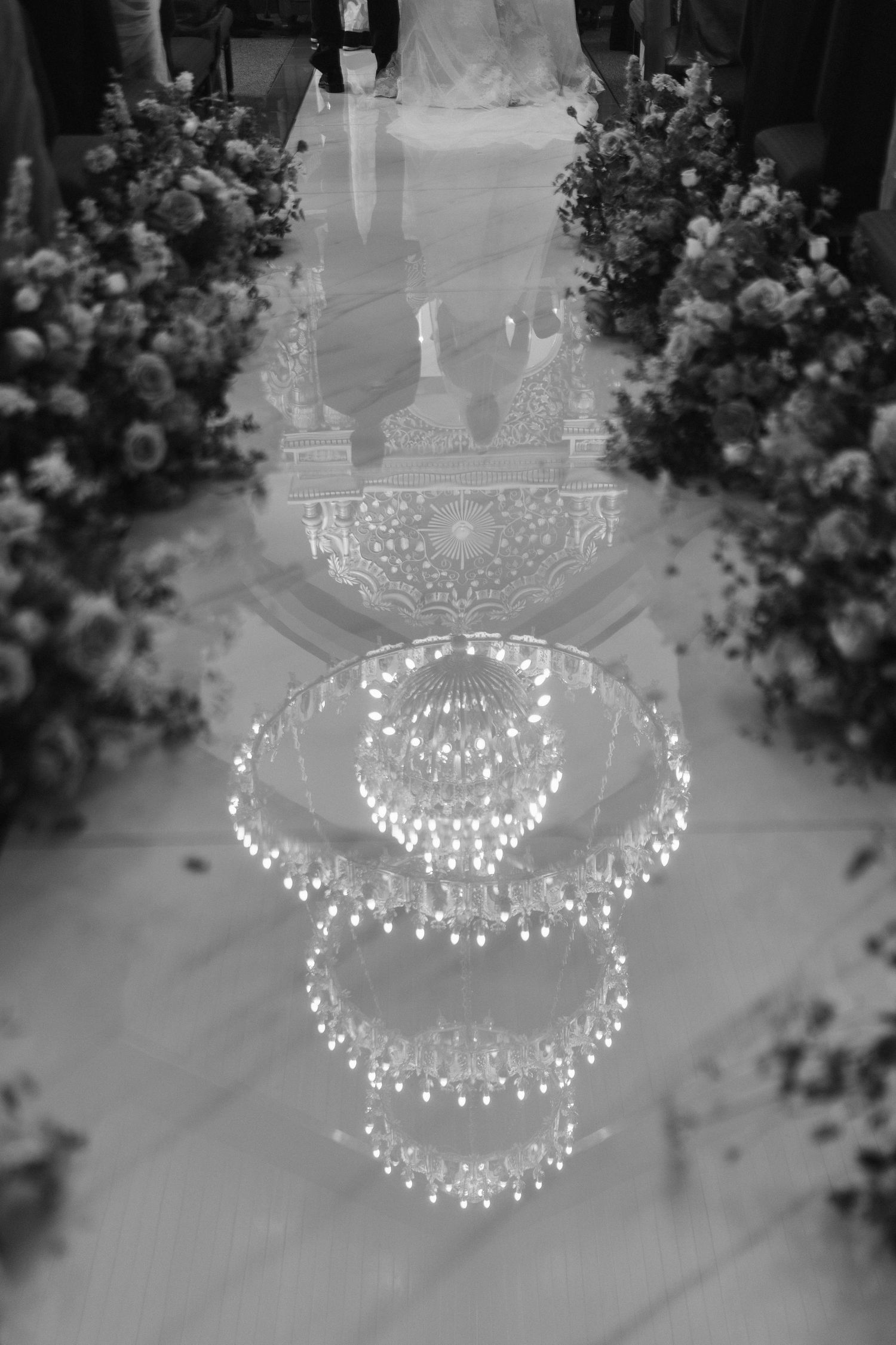 Black and white reflection of crystal chandelier on mirrored wedding aisle with floral arrangements.