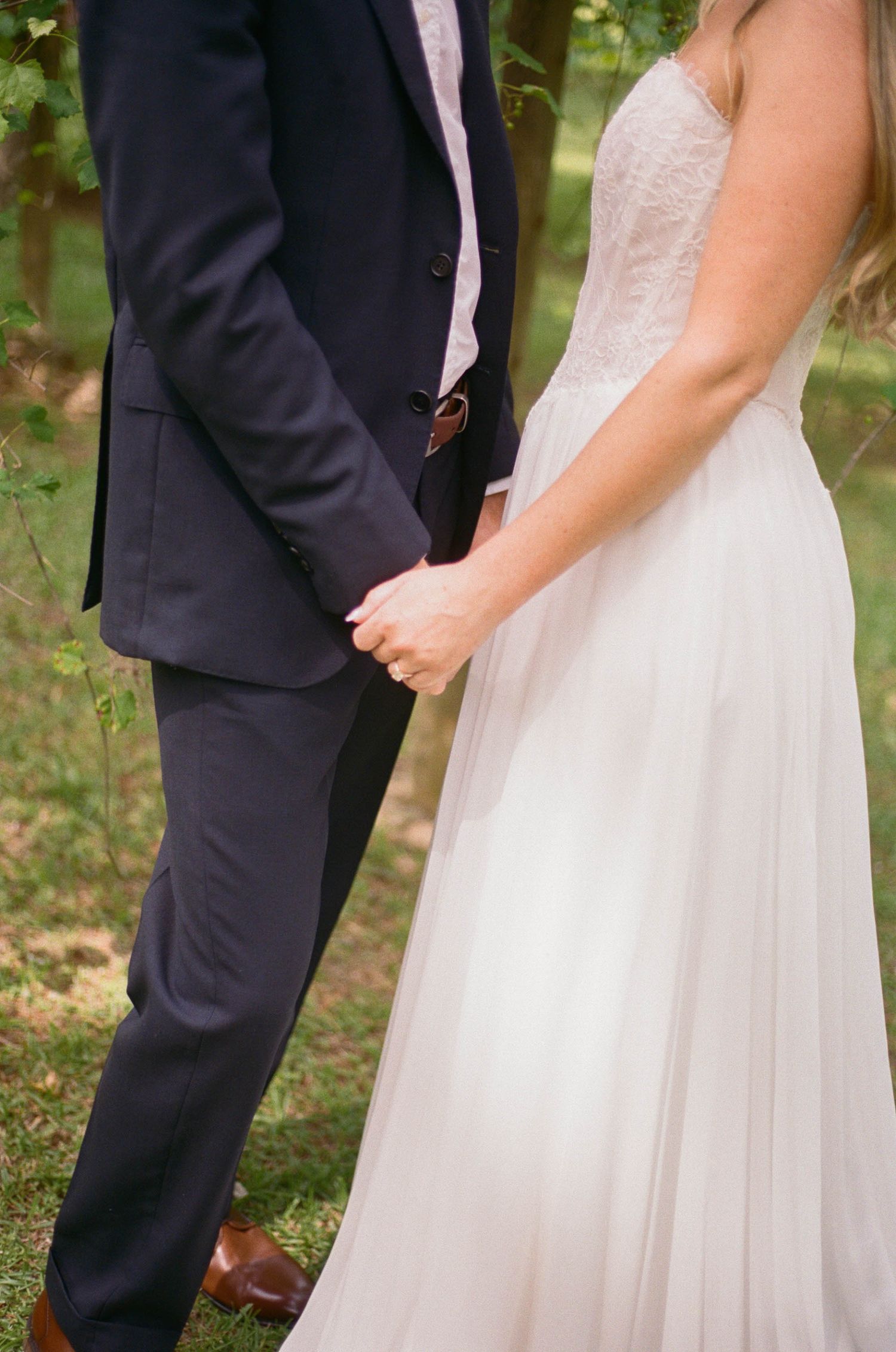 Bride and groom holding hands outdoors, wearing white wedding gown and navy suit.