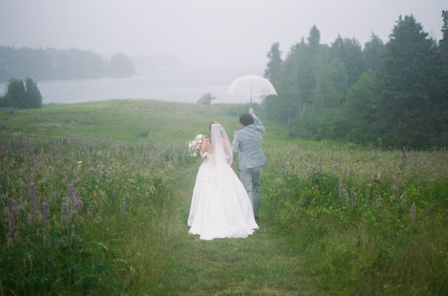 A foggy outdoor wedding ceremony setup with white chairs and decorations in a green meadow.