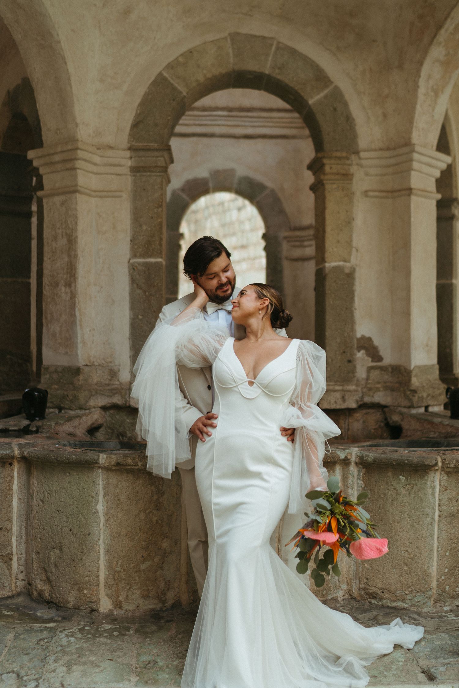 Wedding couple sharing intimate moments under stone archways of a historic building.