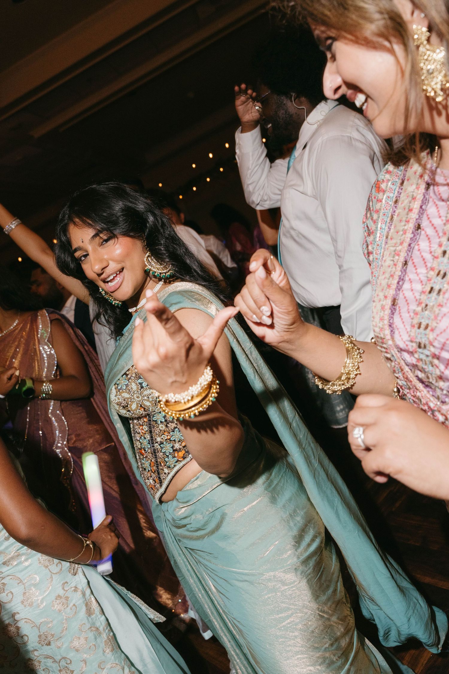 Bride dancing joyfully in mint green lehenga with gold jewelry at wedding reception.