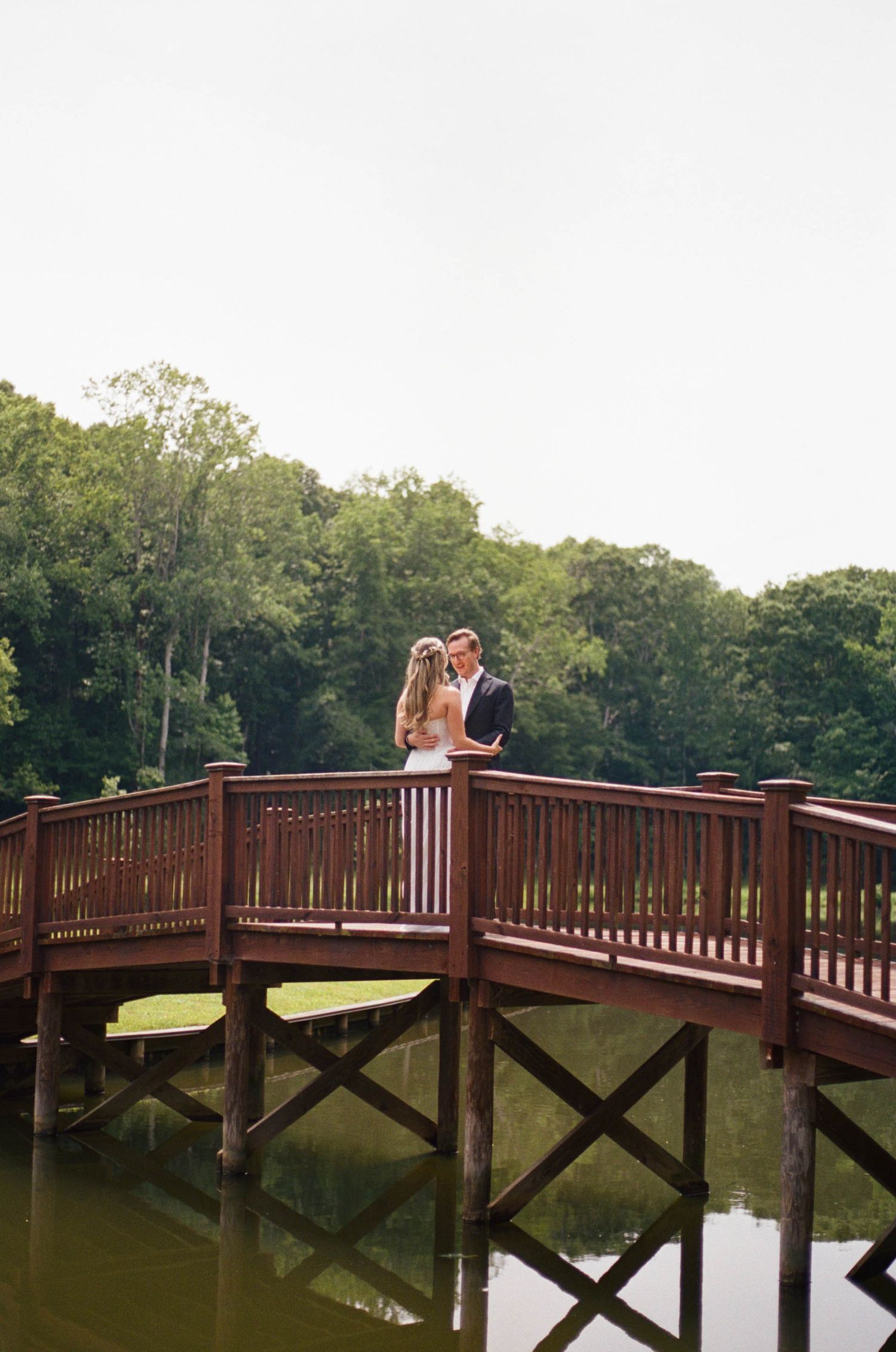 Bride and groom share a romantic moment on a wooden bridge over a serene lake.