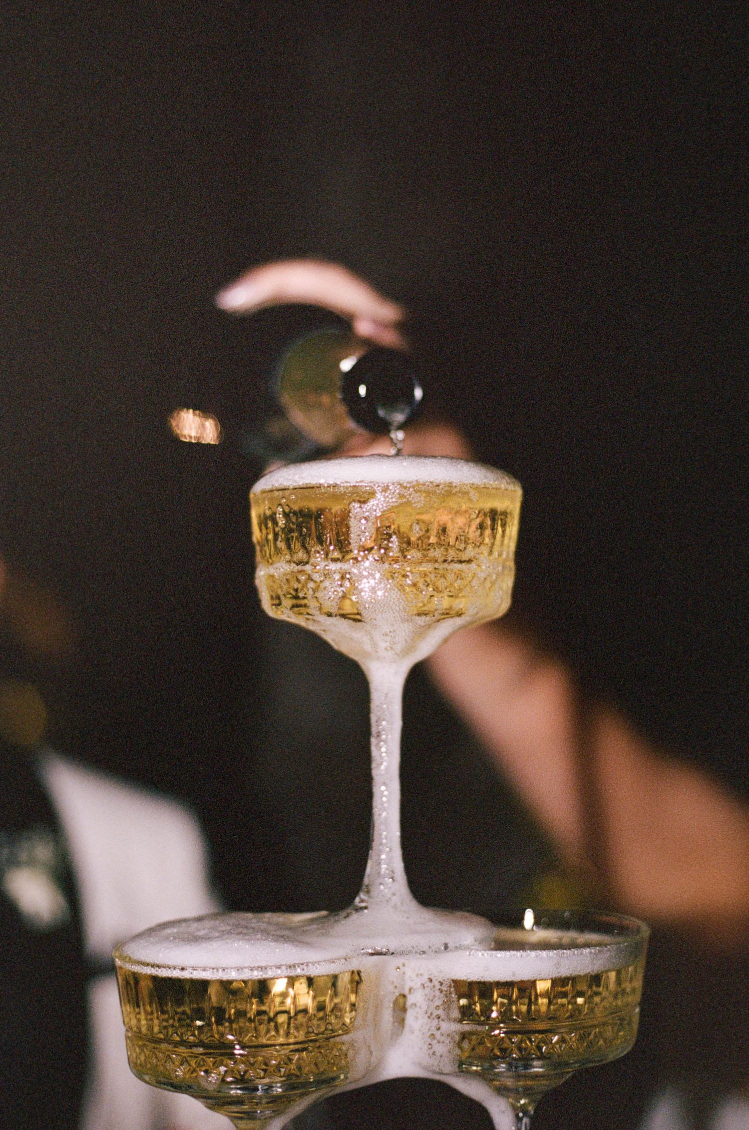 Detailed shot of champagne flowing into vintage-style coupe glasses in a tower formation.