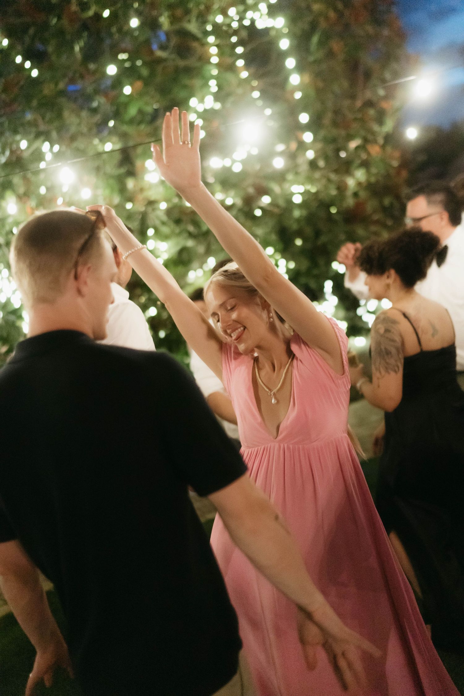 Party guests dancing and celebrating under string lights at an outdoor evening event.
