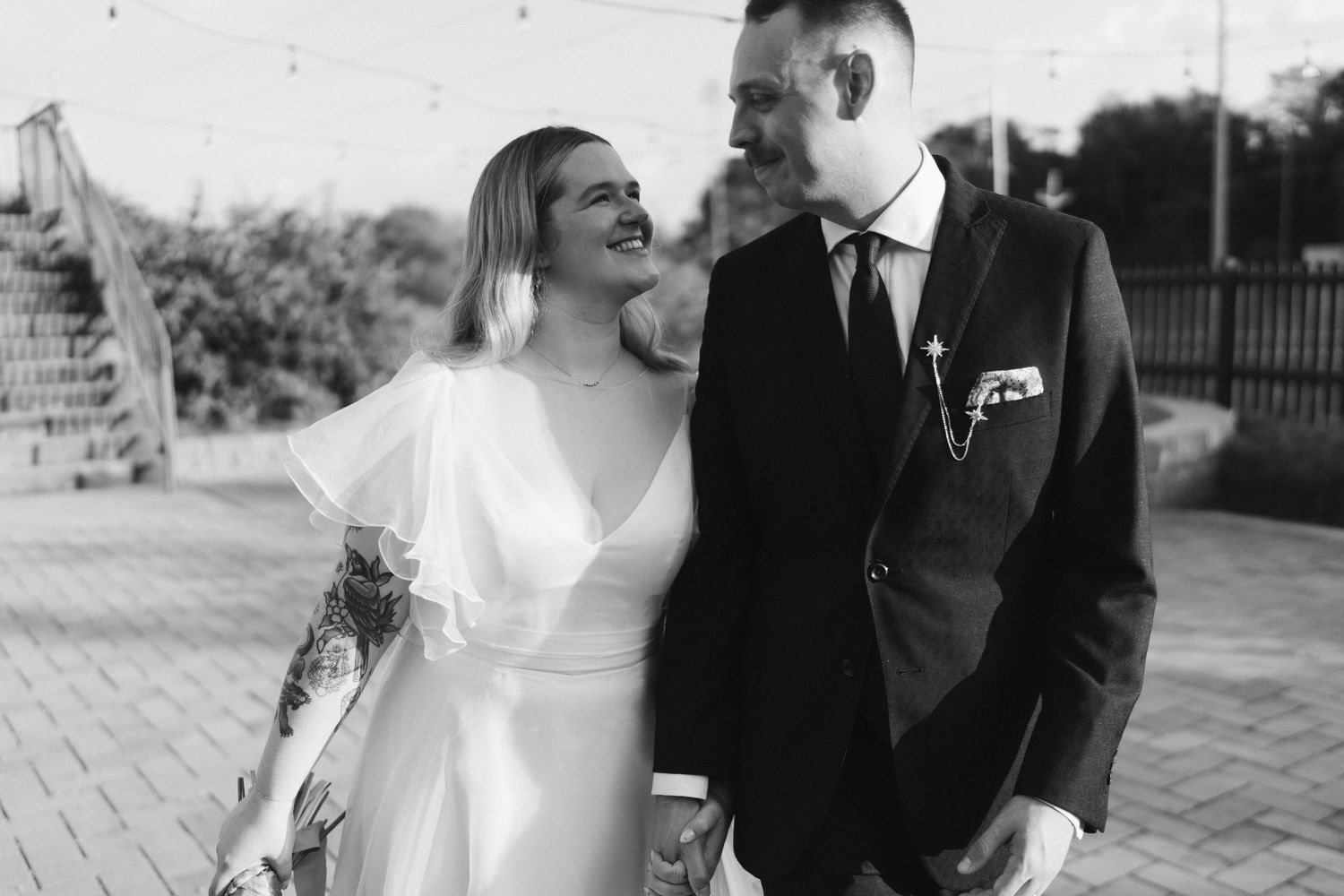 Black and white wedding photo of a couple laughing together outdoors on a brick path.