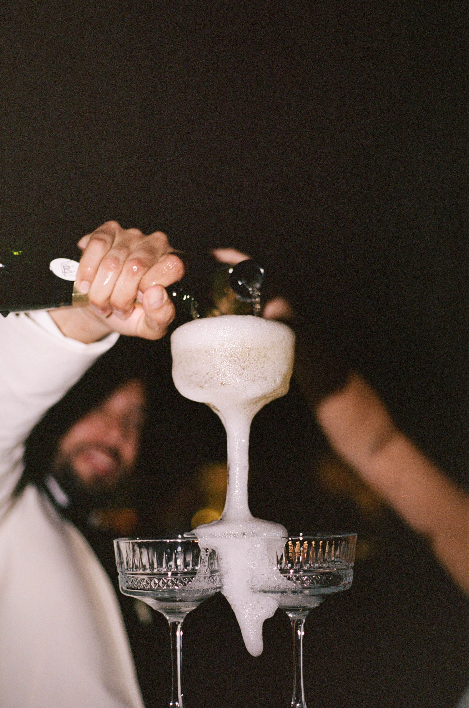 Champagne being poured into a tower of vintage-style coupe glasses creating a cascading effect.