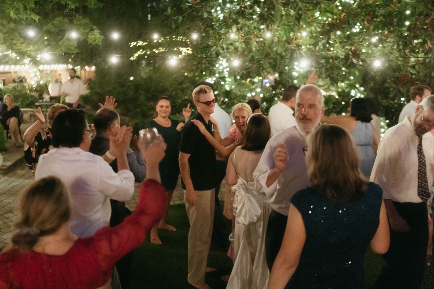 People dancing and celebrating at a nighttime wedding reception under illuminated trees.