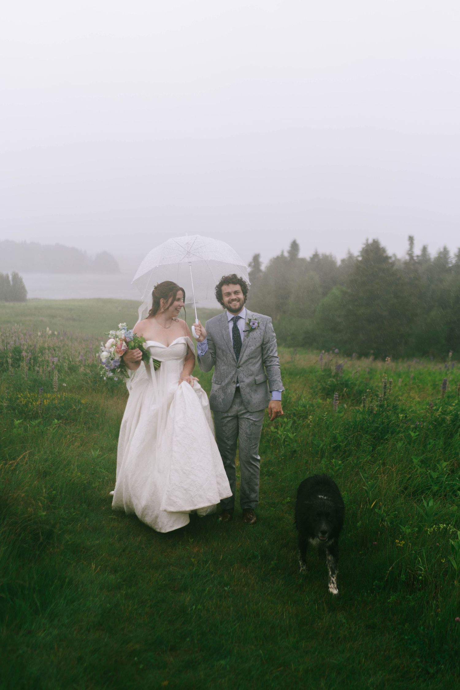 Wedding couple strolls through tall grass on a foggy hillside.