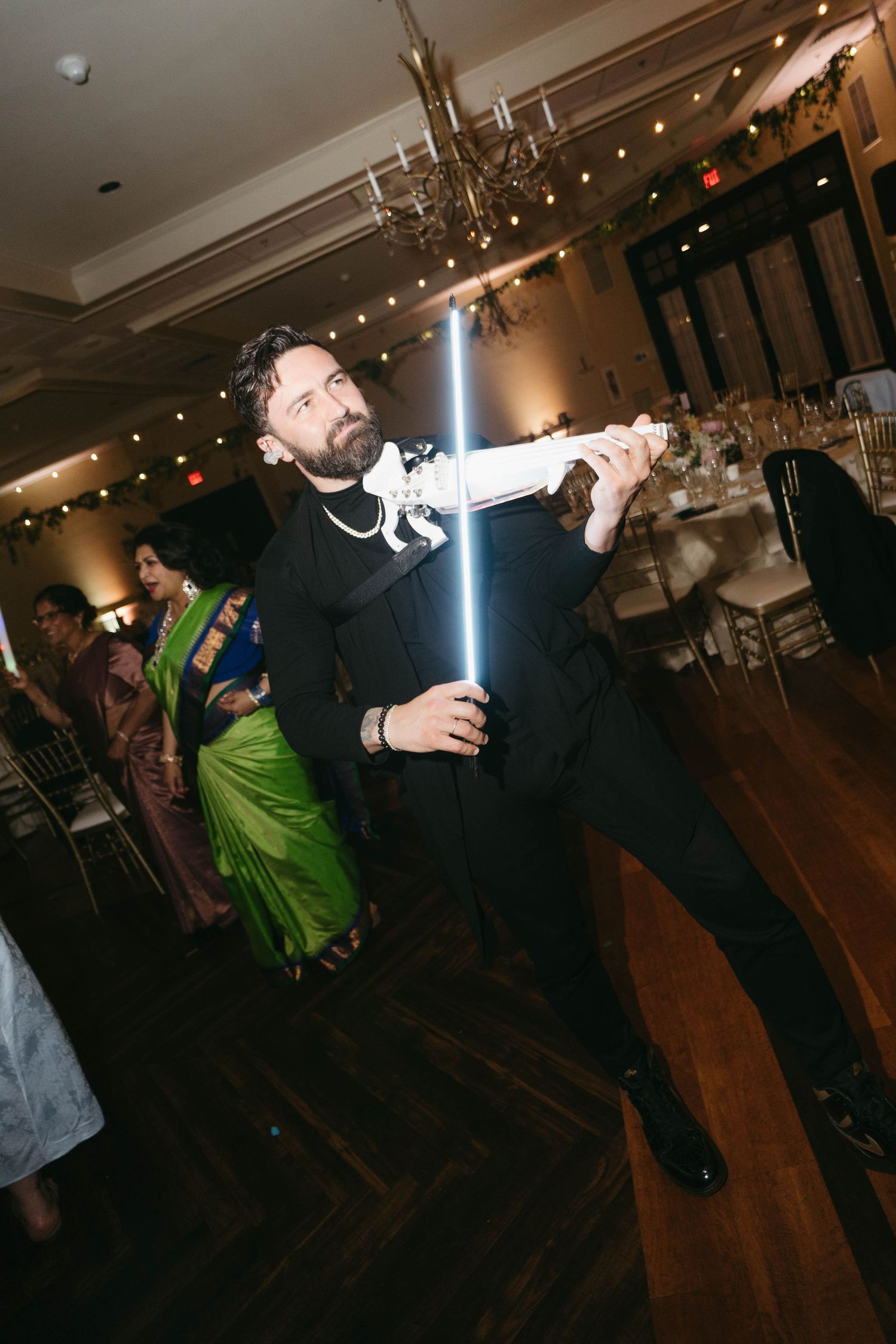 Man in black suit wielding a glowing blue lightsaber at an elegant wedding reception venue.