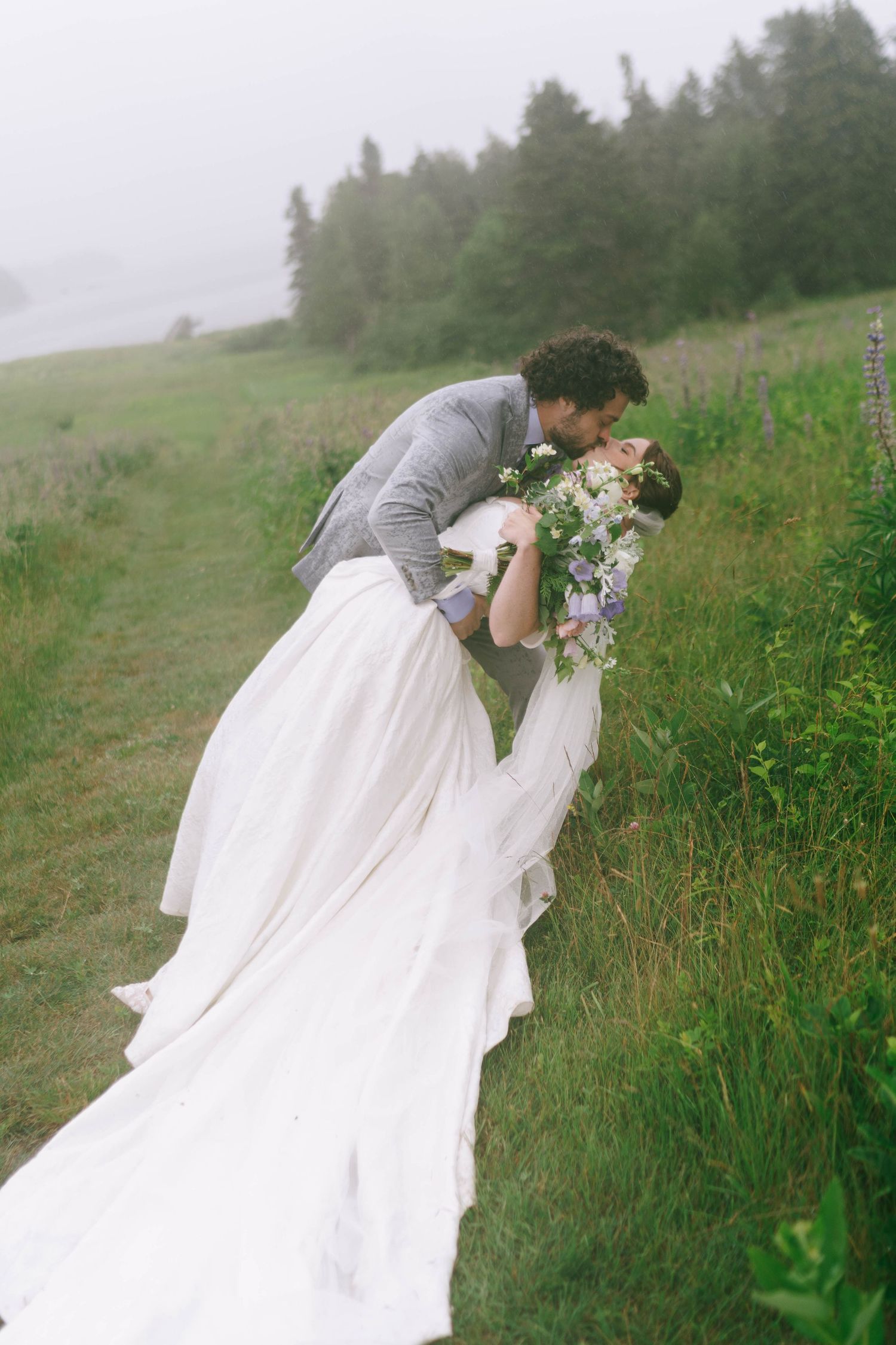 A wedding couple poses in a foggy meadow with flowing white dress and grey suit.