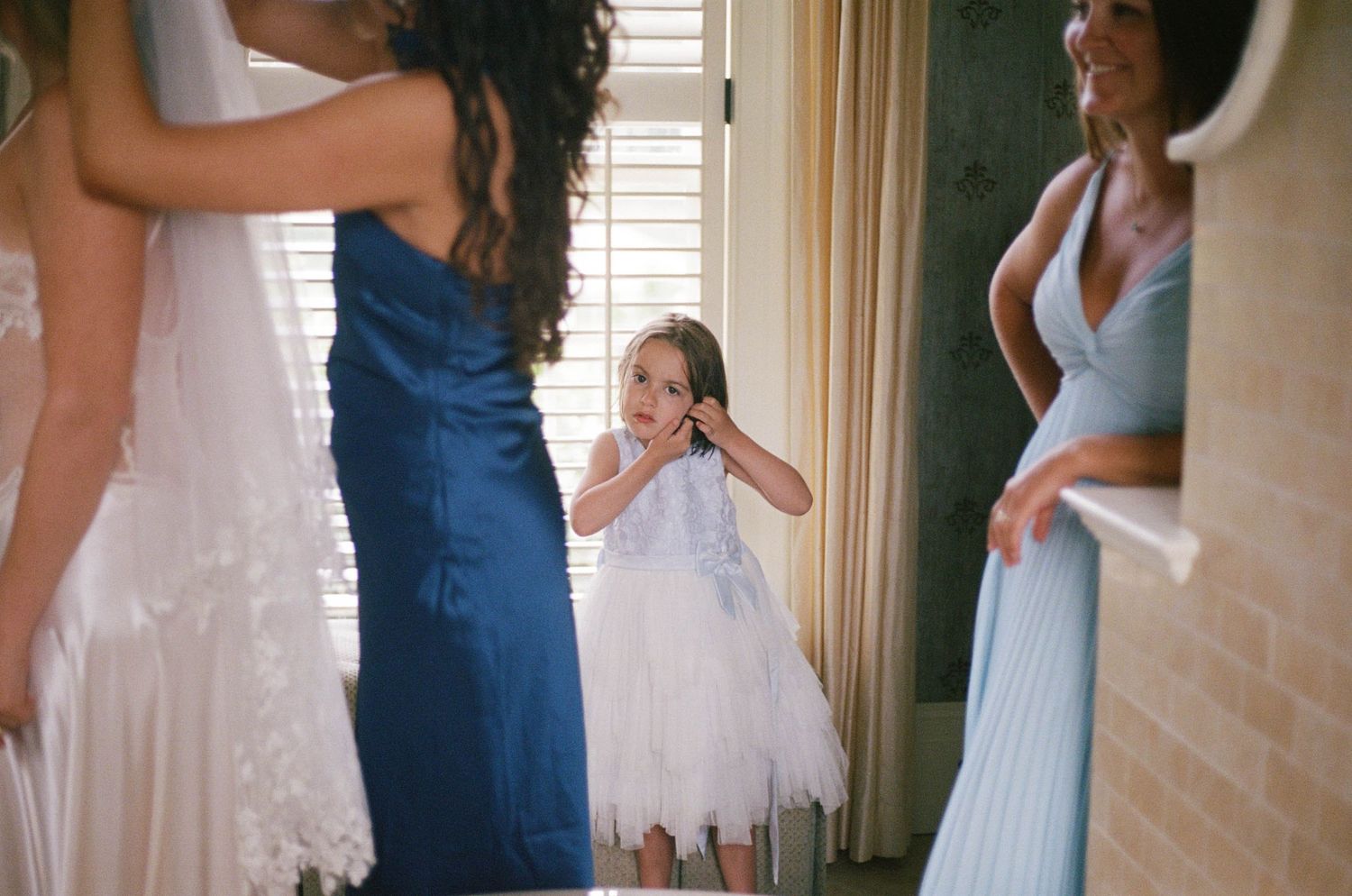 Adorable flower girl in white tutu dress smiling among bridesmaids in blue gowns before wedding.