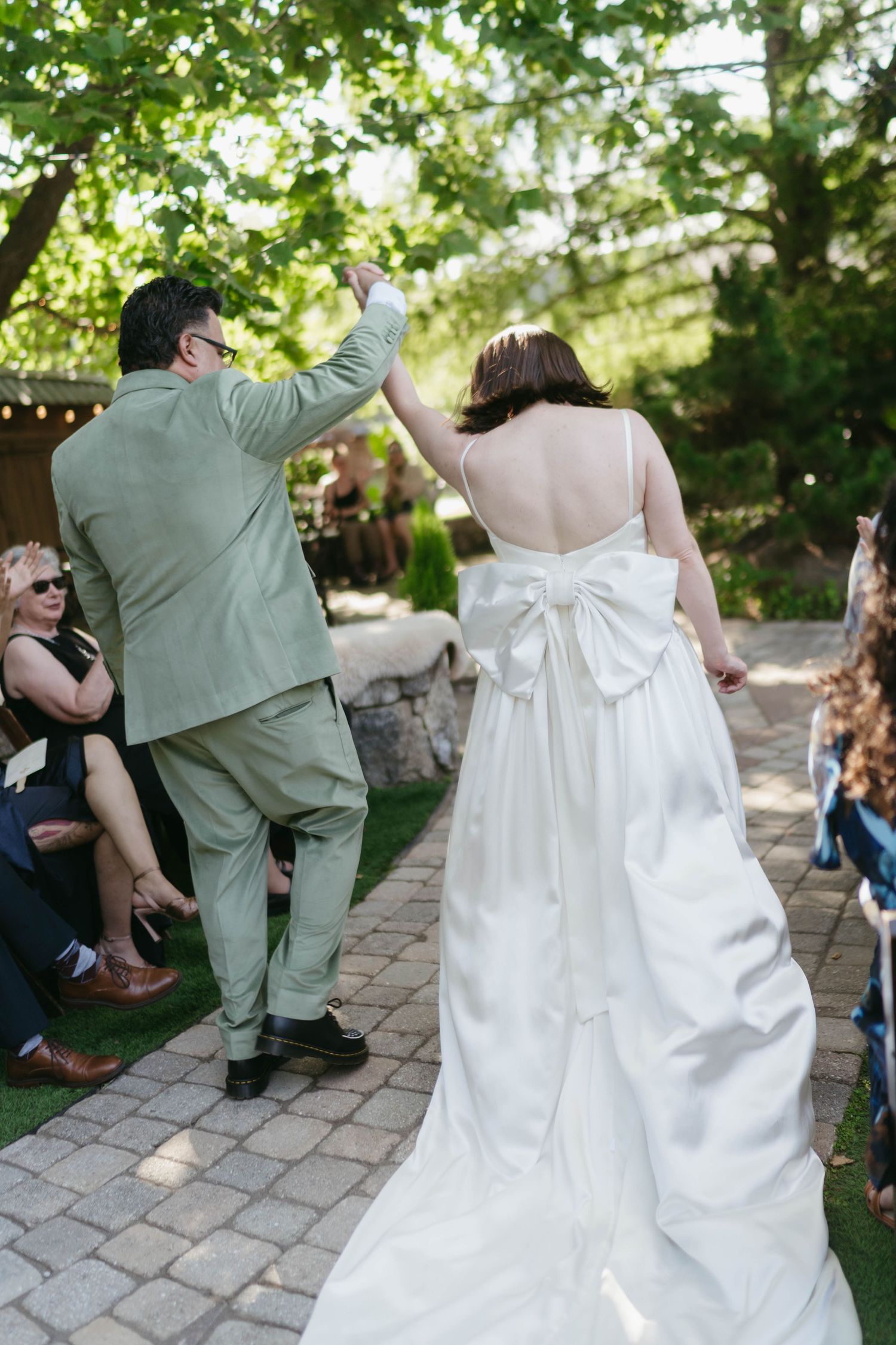 Back view of a wedding dress with a large bow detail as couple walks on stone pathway.