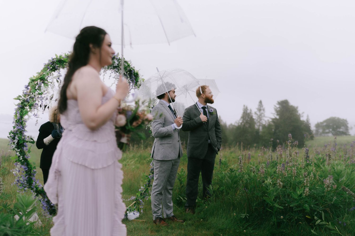 An outdoor wedding ceremony under a floral arch in a misty field.