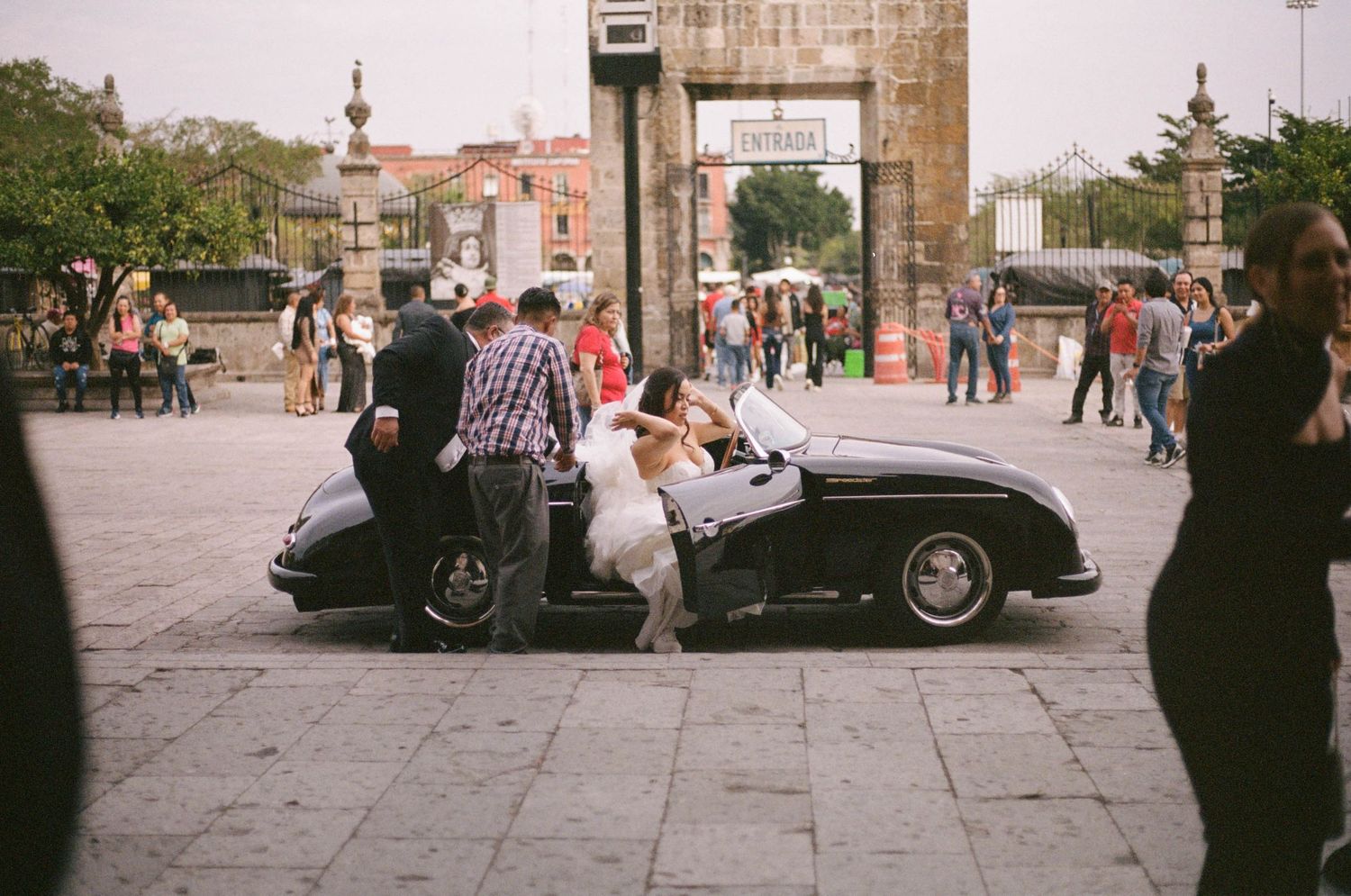 Vintage cars parked outside a historic stone building with wedding guests milling about.