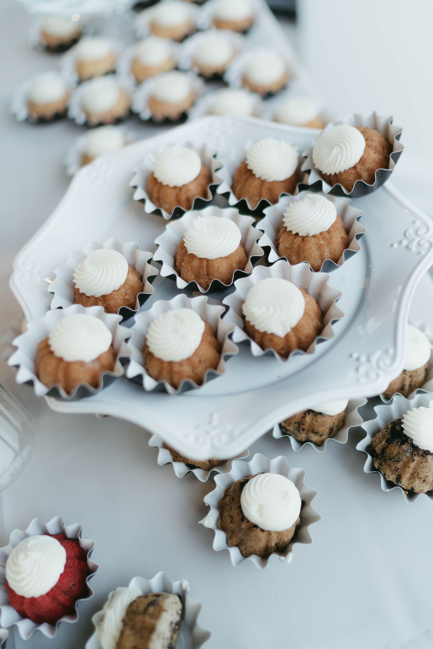 Mini bundt cakes with white frosting displayed on an ornate white serving platter.