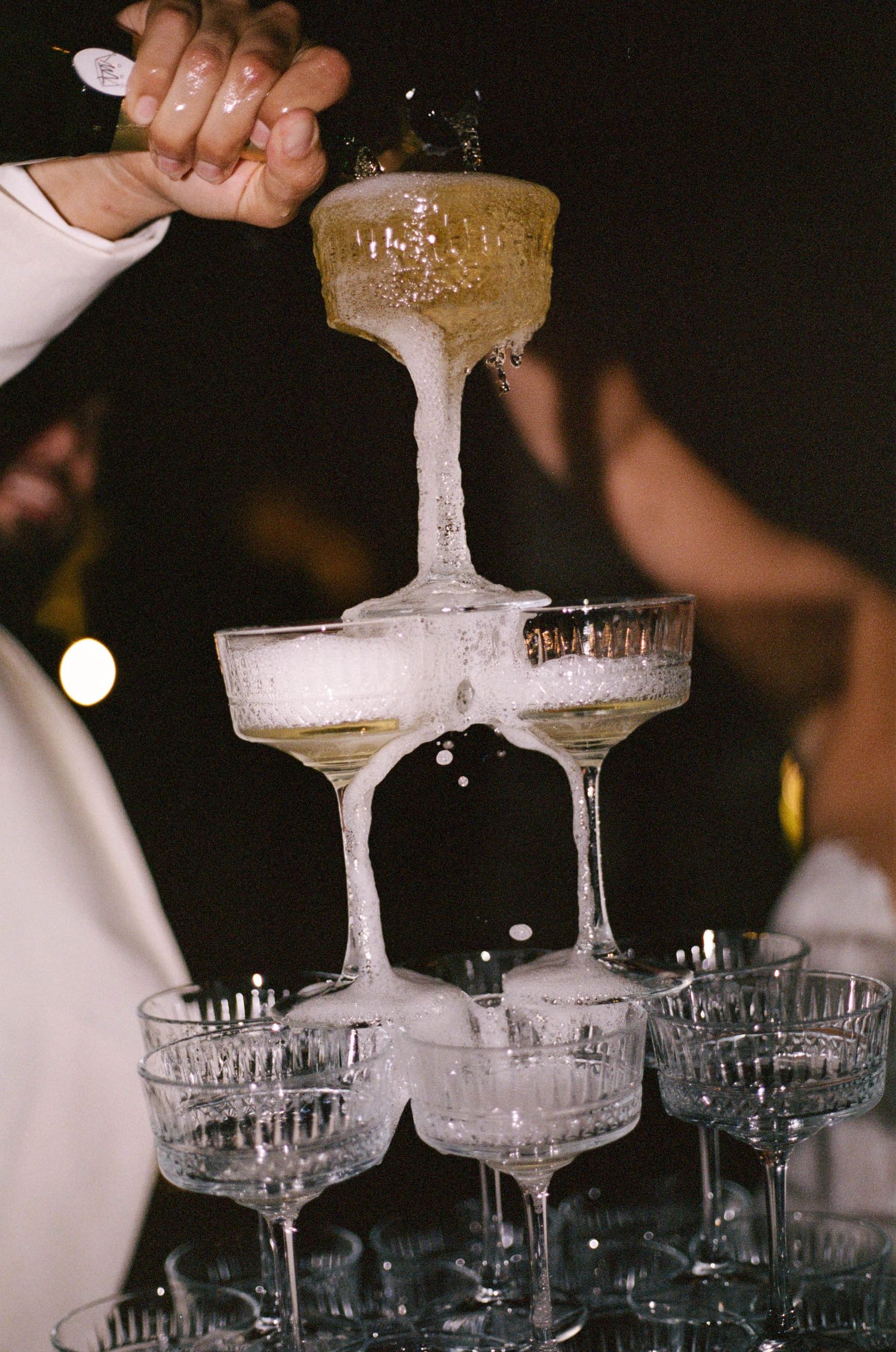 Champagne being poured into a tower of stacked crystal glasses creating an elegant cascade effect.