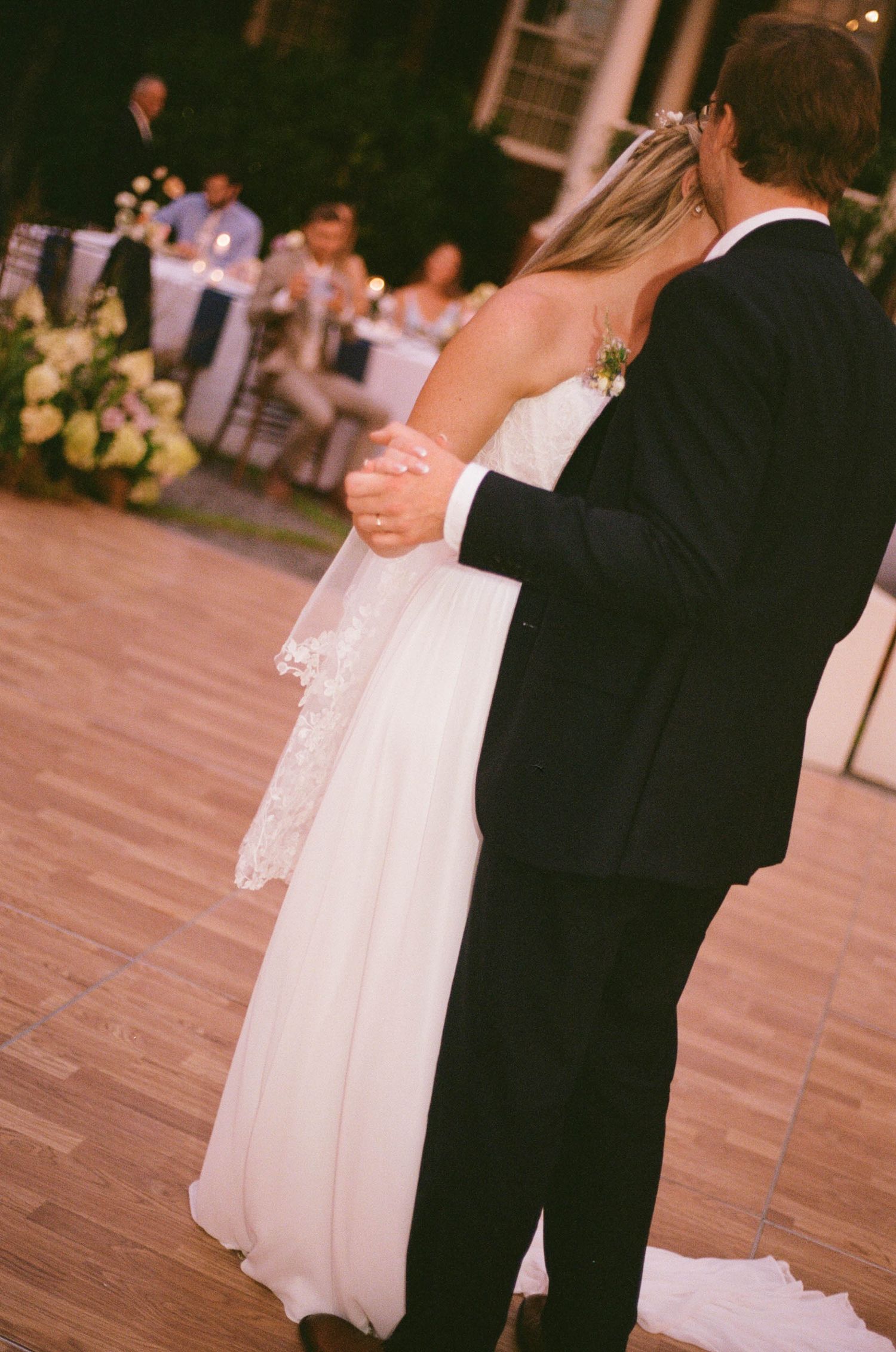 Bride and groom sharing their first dance on a wooden floor at an evening wedding reception.