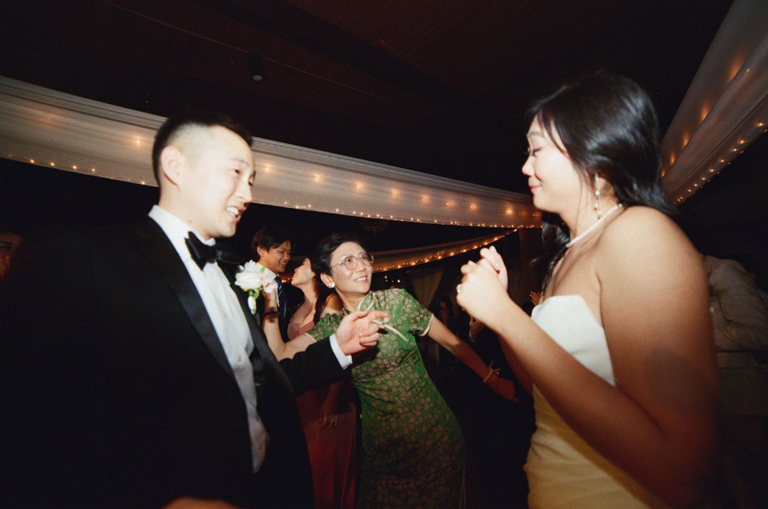 Dimly lit wedding reception scene with string lights and dancing silhouettes.