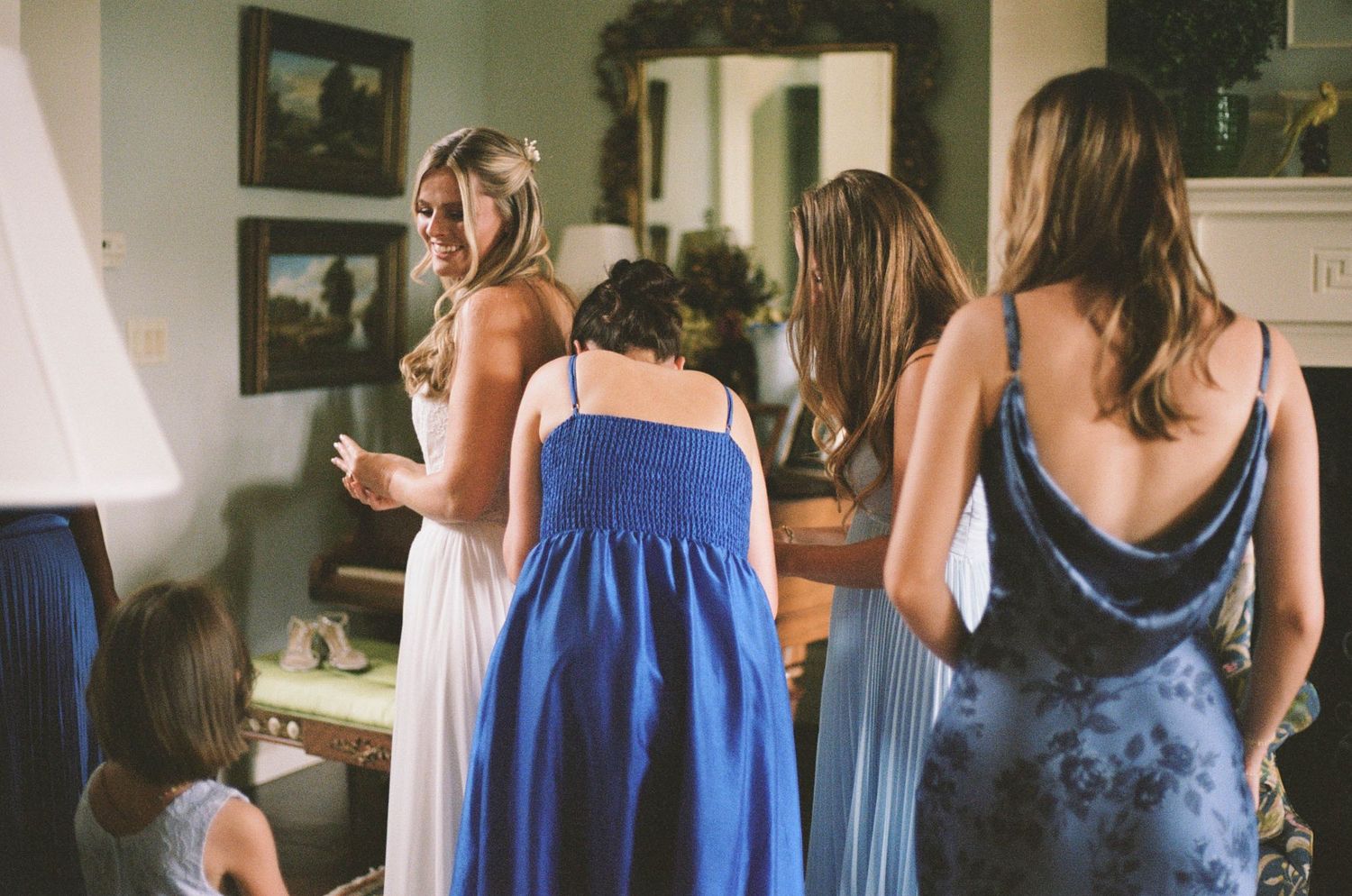 Bridesmaids in blue dresses gather around bride during wedding preparation indoors.