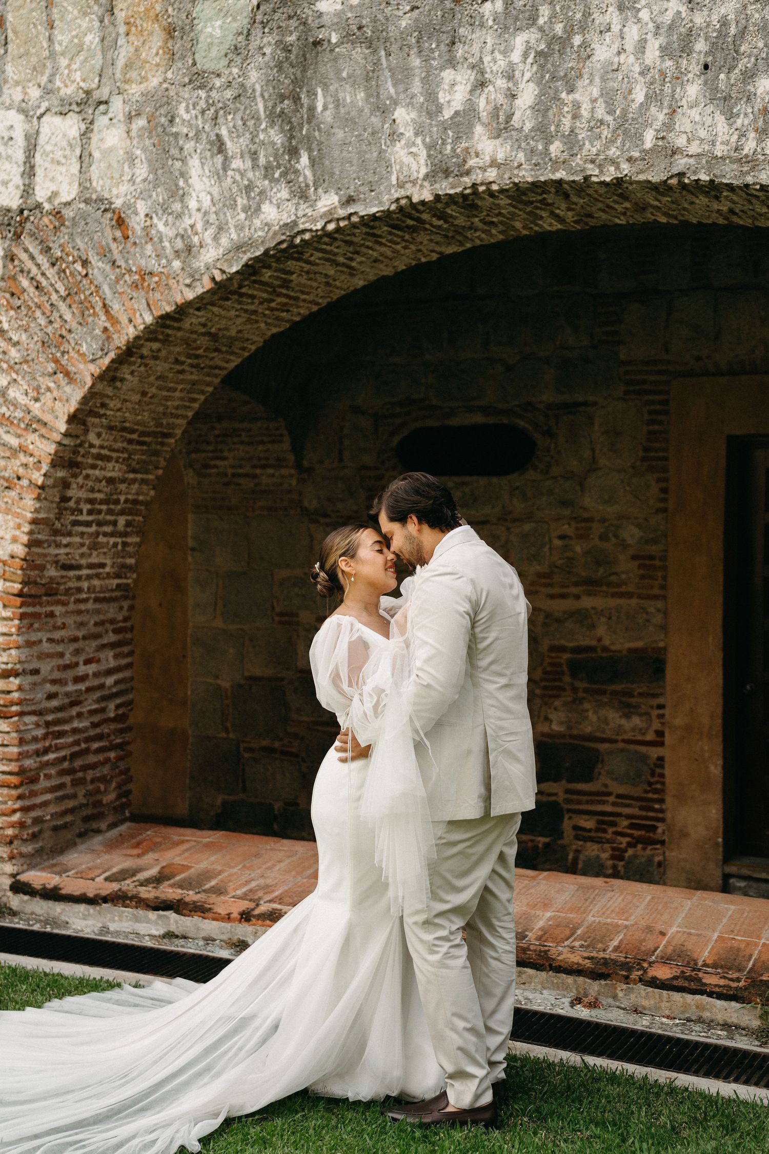 A romantic wedding moment under a brick archway with flowing white dress and veil.