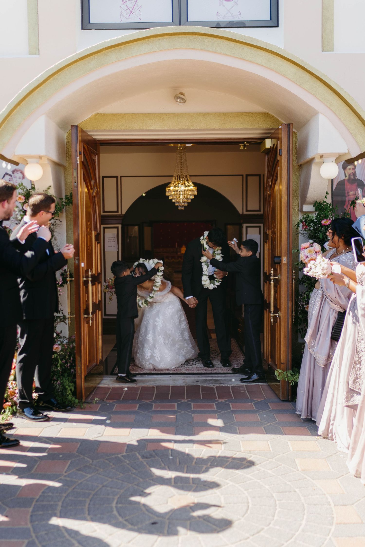 Newlyweds exit church doors as guests celebrate their wedding ceremony with flower petals and applause.