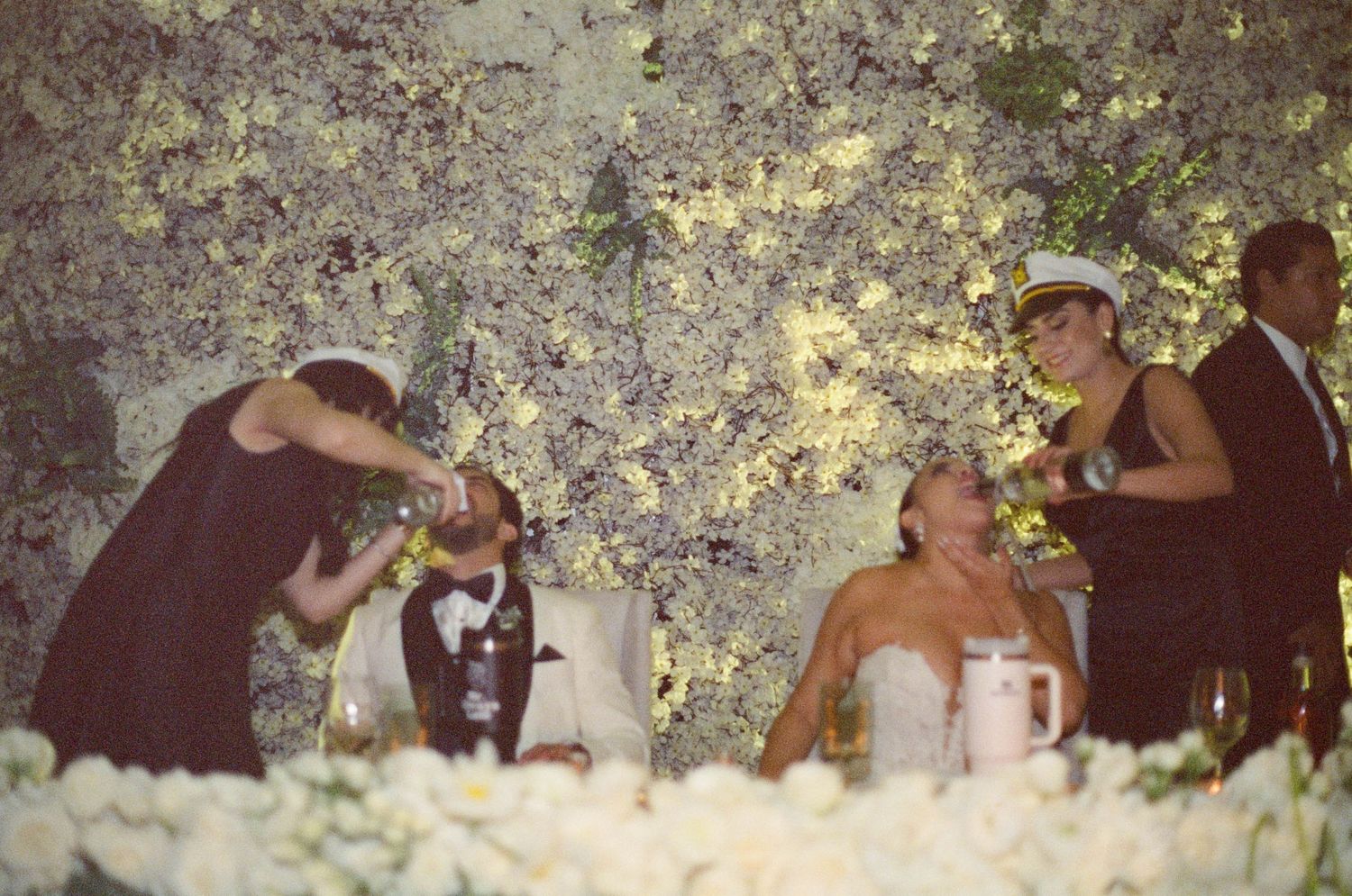 Wedding guests celebrate with drinks at an outdoor reception under trees.