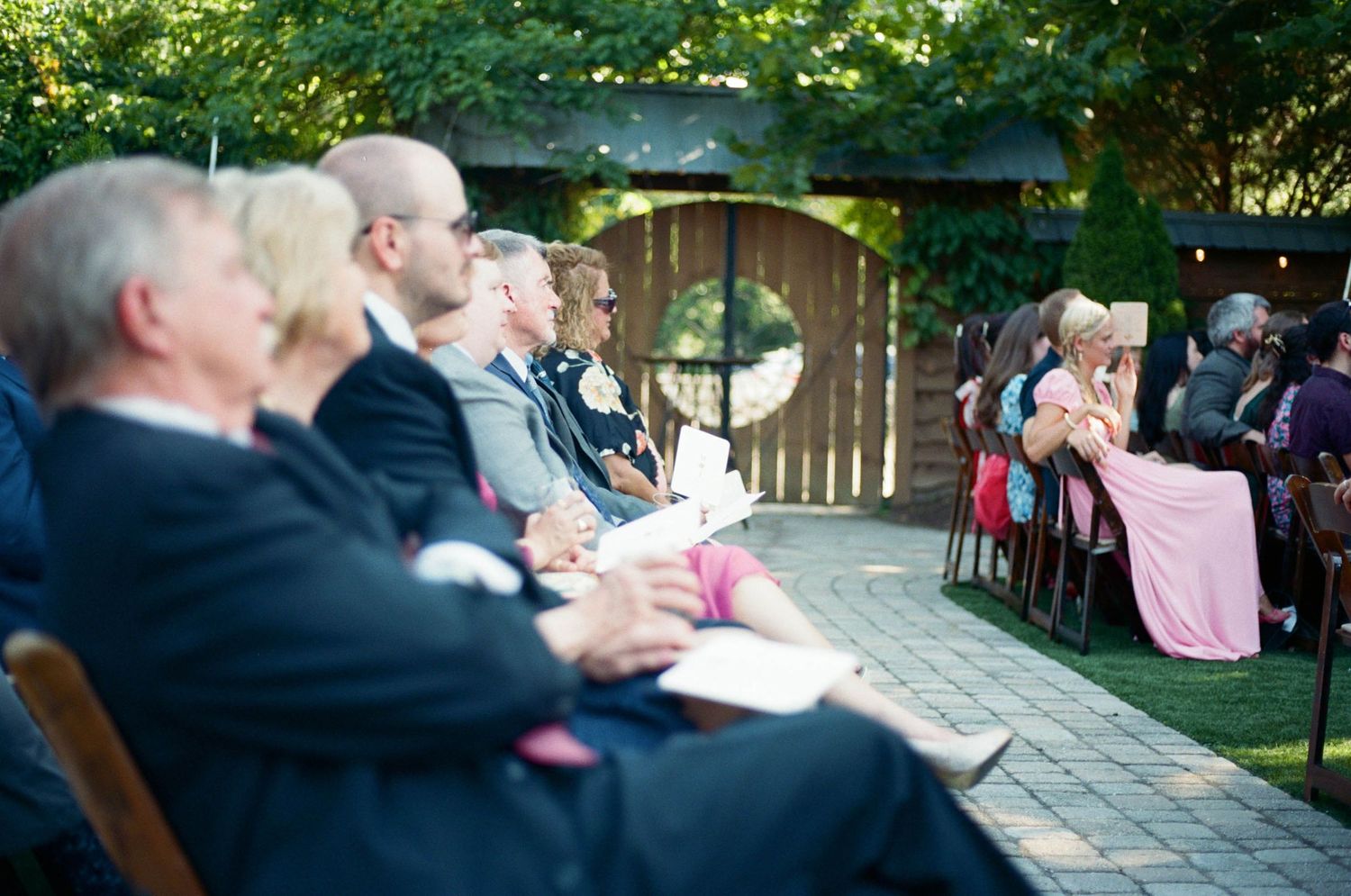 Wedding guests seated on wooden chairs watch the ceremony proceedings.