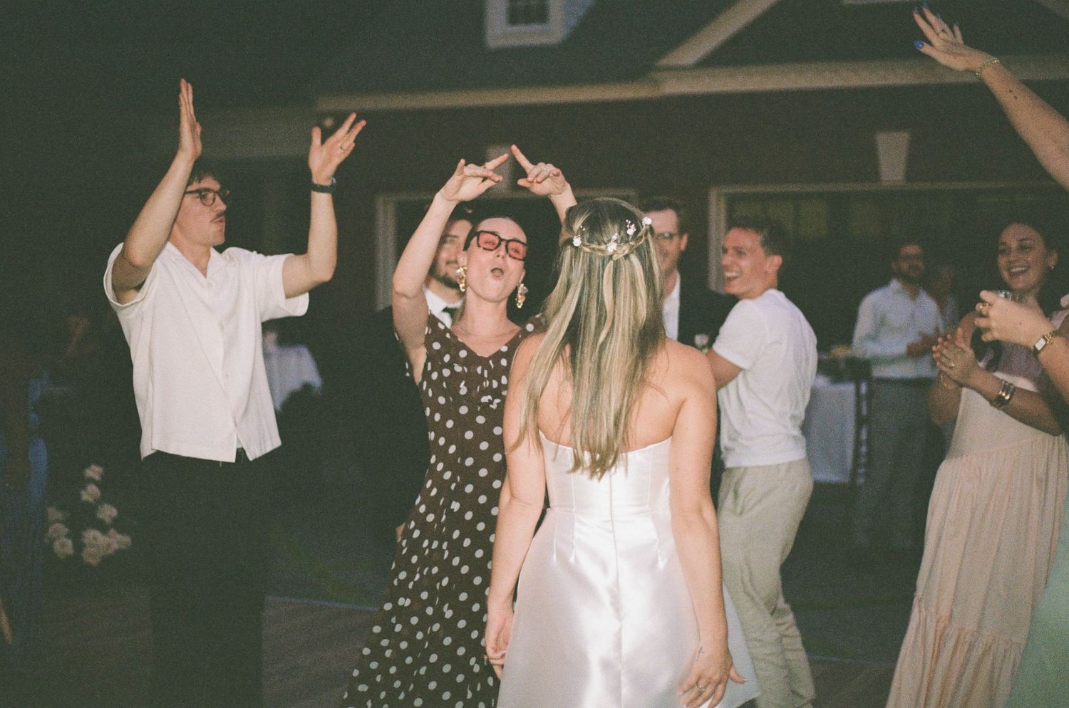 Bride in white dress dances joyfully with a guest in a polka dot dress at wedding reception.