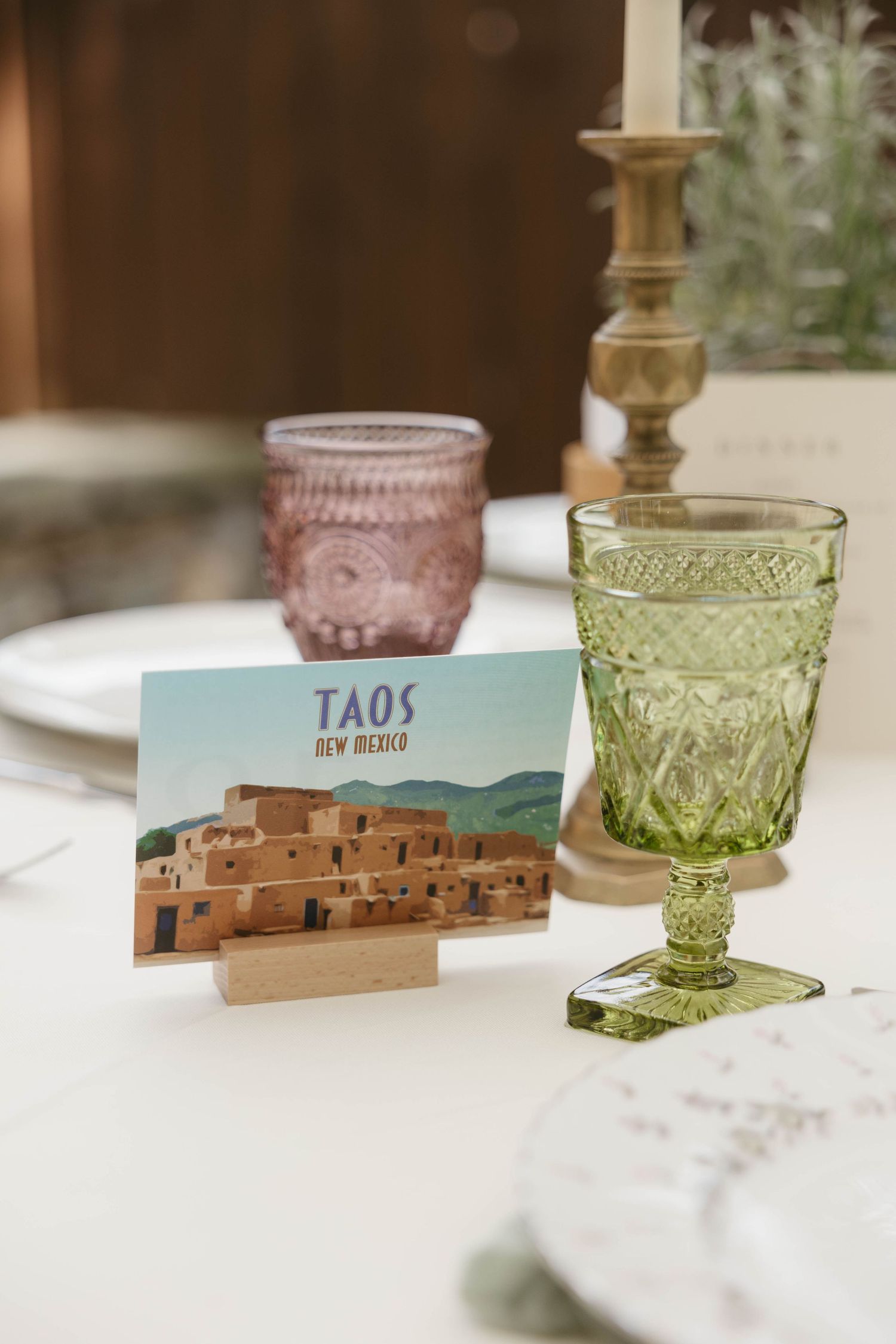 Vintage-style colored glass goblets with Taos pueblo place cards on white tablecloth.