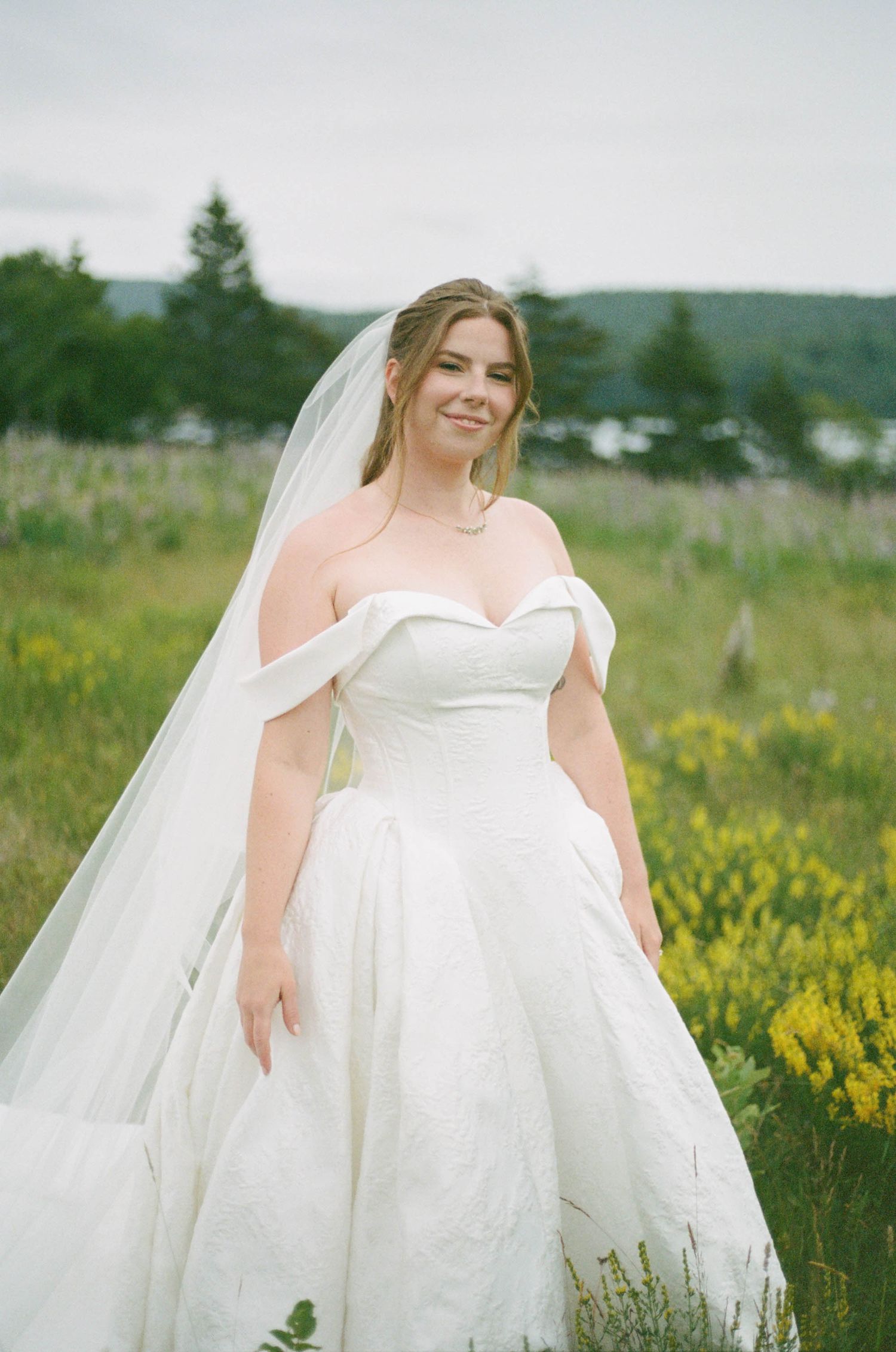 A bride in a flowing white wedding dress twirls in a field of yellow wildflowers on a summer day.