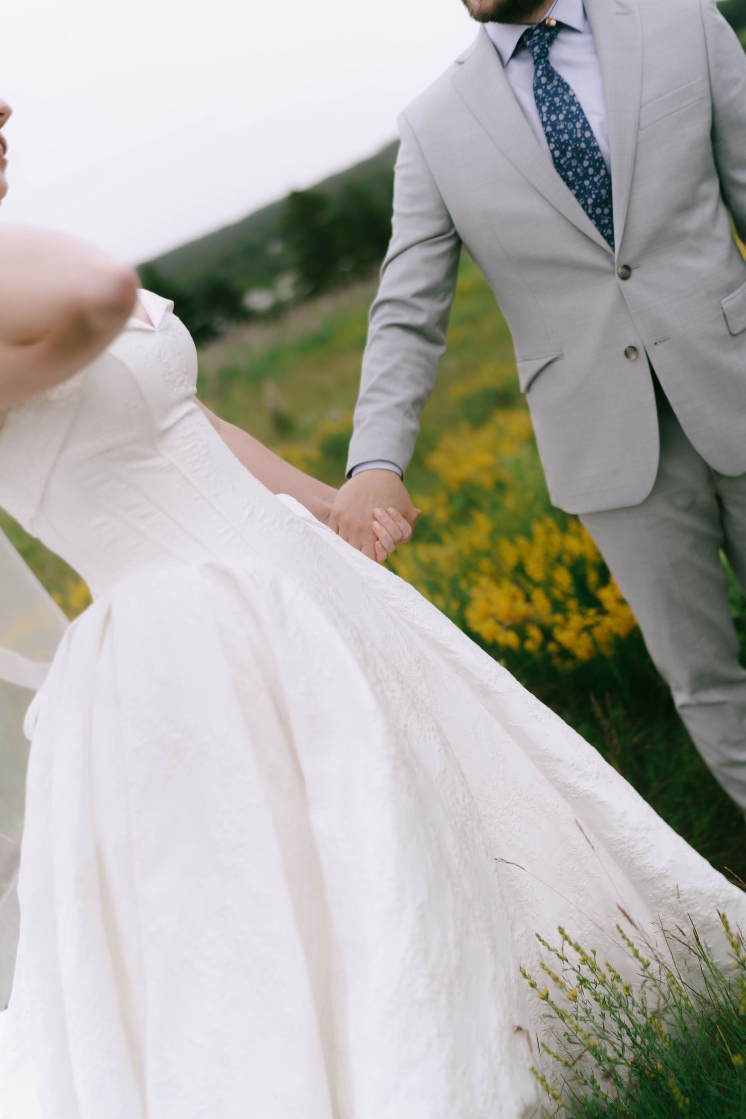 A flowing white wedding dress and grey suit are captured in motion against a natural landscape.