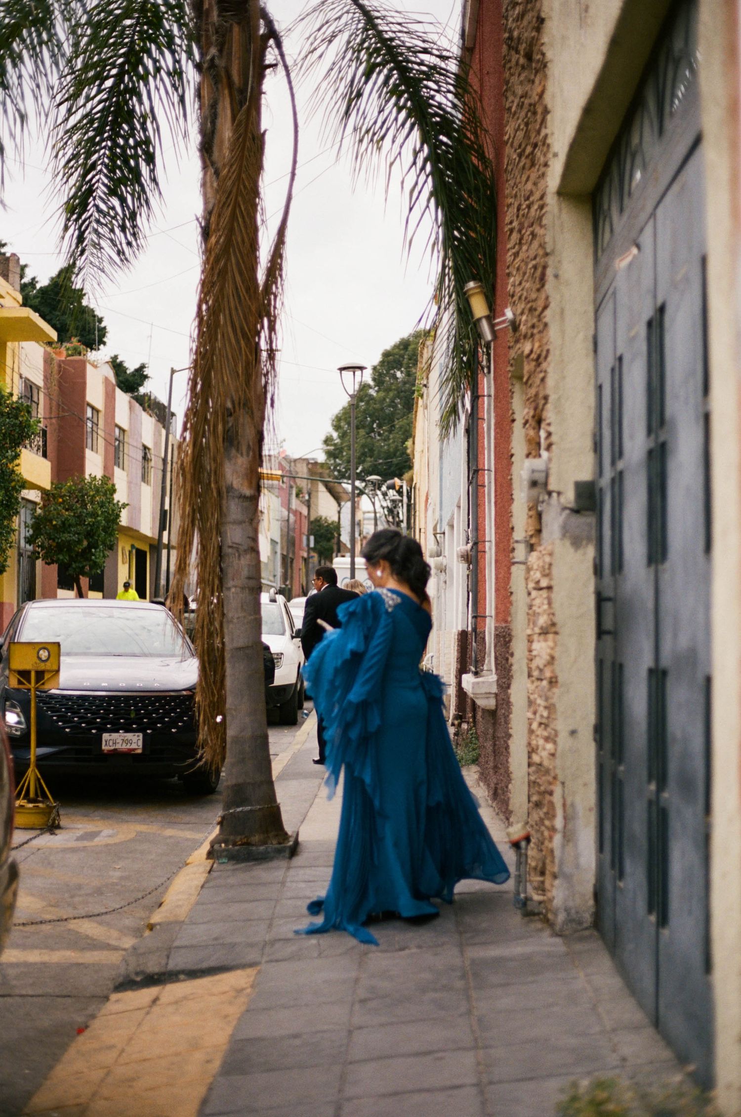 People in blue outfits walking along a palm tree-lined street.