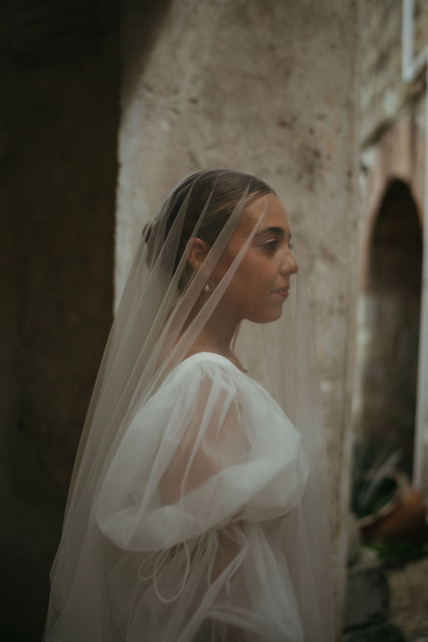 An artistic side profile portrait of a bride in a flowing white dress with sheer veil.
