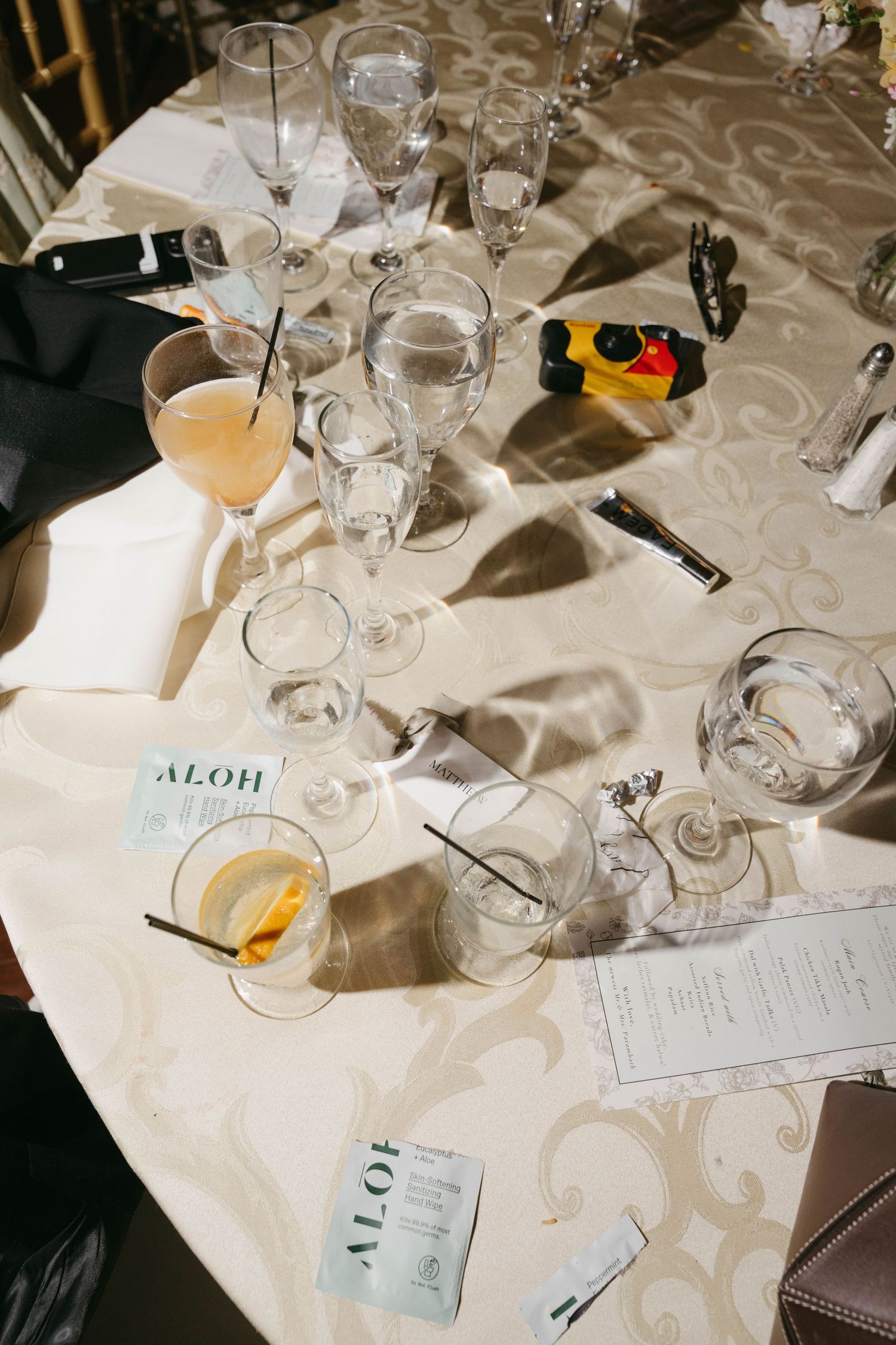Overhead view of wedding reception table with cocktail glasses, menus, and floral tablecloth after celebration.