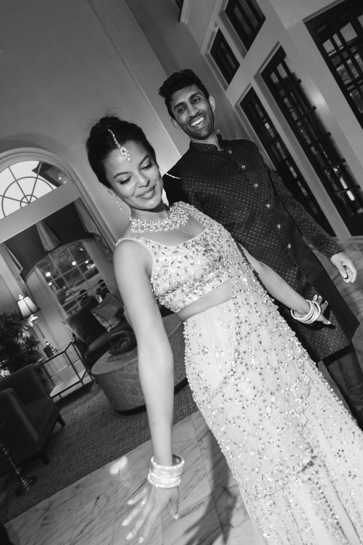 Indian couple in traditional attire dancing elegantly at a wedding reception in black and white.