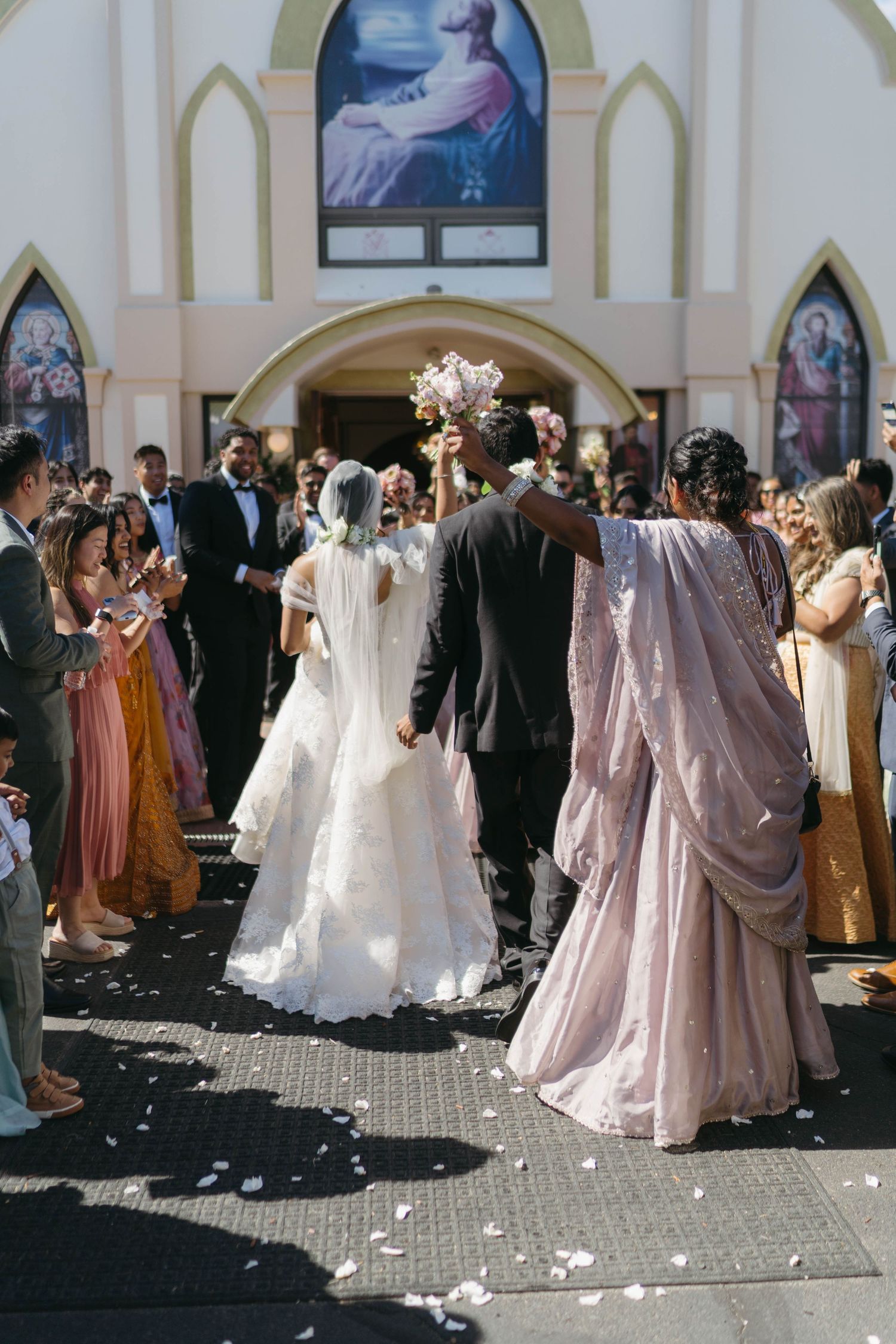 Bride and groom exit a church ceremony as guests celebrate with flower petals and applause.