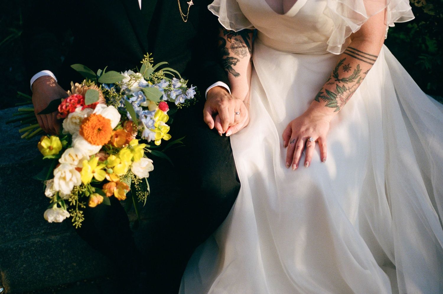 Wedding bouquets with yellow and orange flowers held against white dresses.