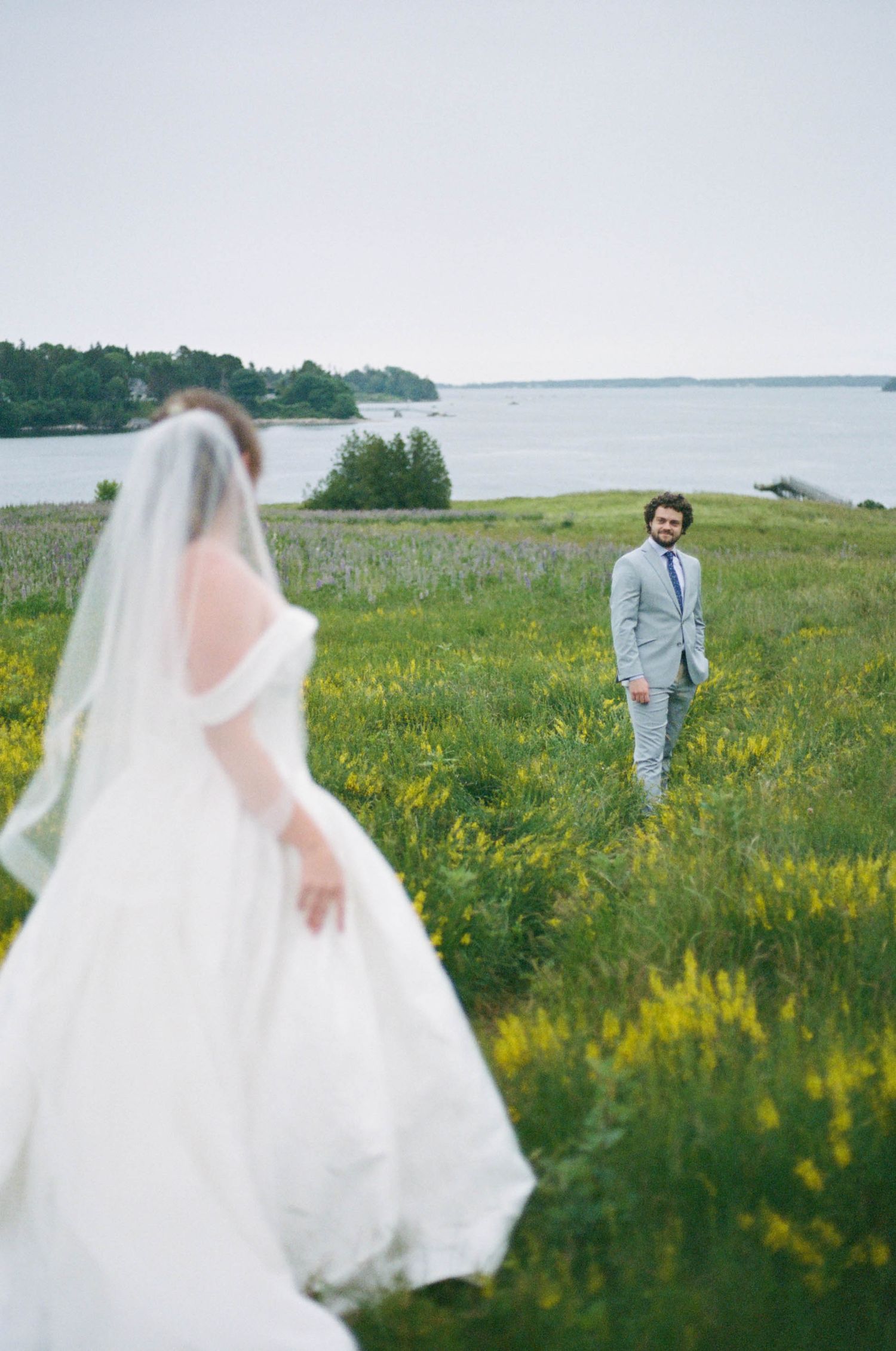 A romantic first look moment between newlyweds in a coastal meadow filled with yellow flowers.